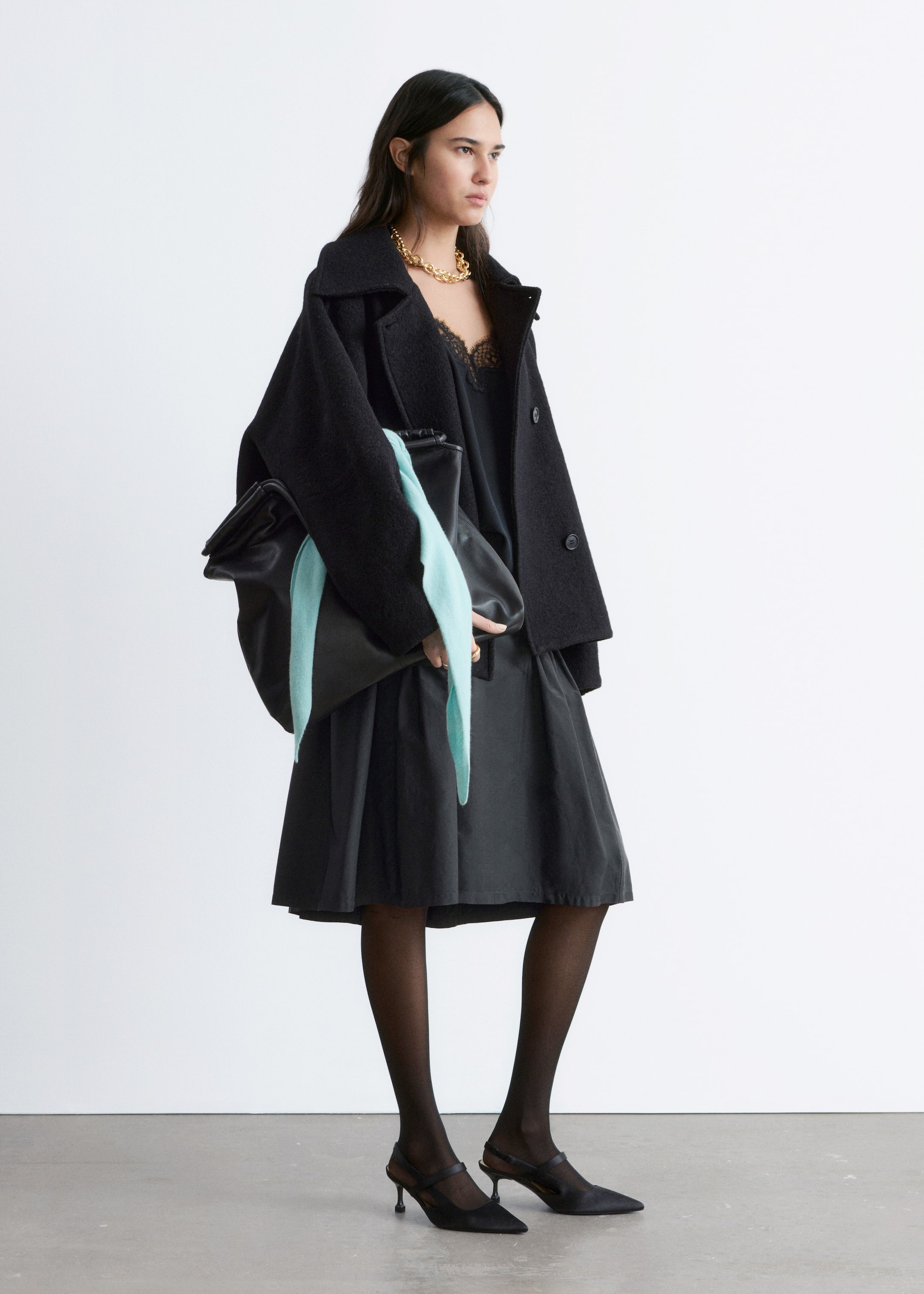 Grösseres Bild ansehen: Ein schwarzer, strukturierter Mantel wird aus einem leichten Seitenwinkel präsentiert, mit einem breiten Kragen, zwei sichtbaren Frontknöpfen, weiten Ärmeln und einer offenen Vorderseite. Er zeigt eine entspannte Passform in mittlerer Oberschenkellänge.