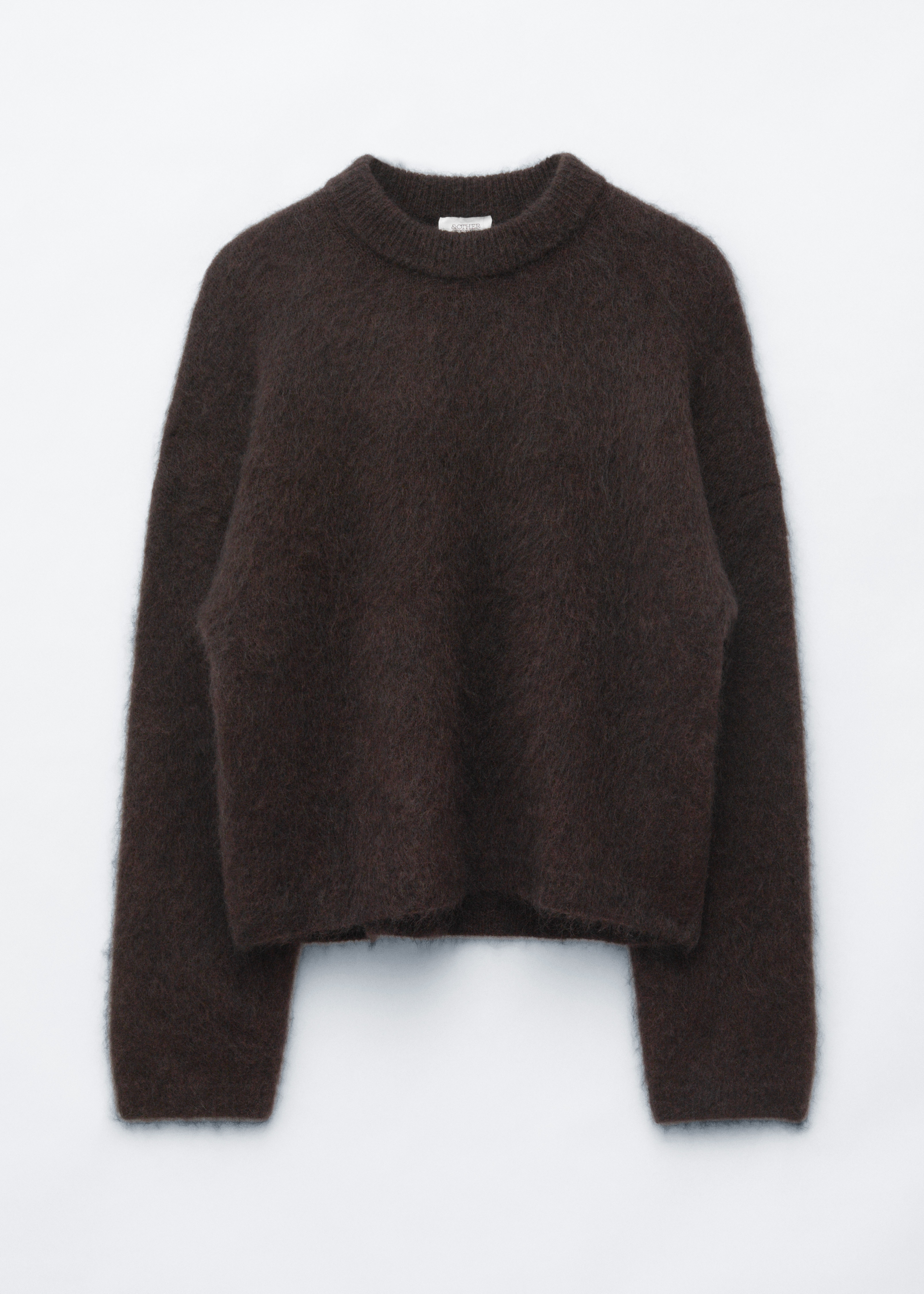 A dark brown mohair-blend jumper with a fuzzy, textured finish and a crew neck is being worn by the model. The jumper is styled with matching dark brown trousers, and the model is carrying a dark brown leather shoulder bag.