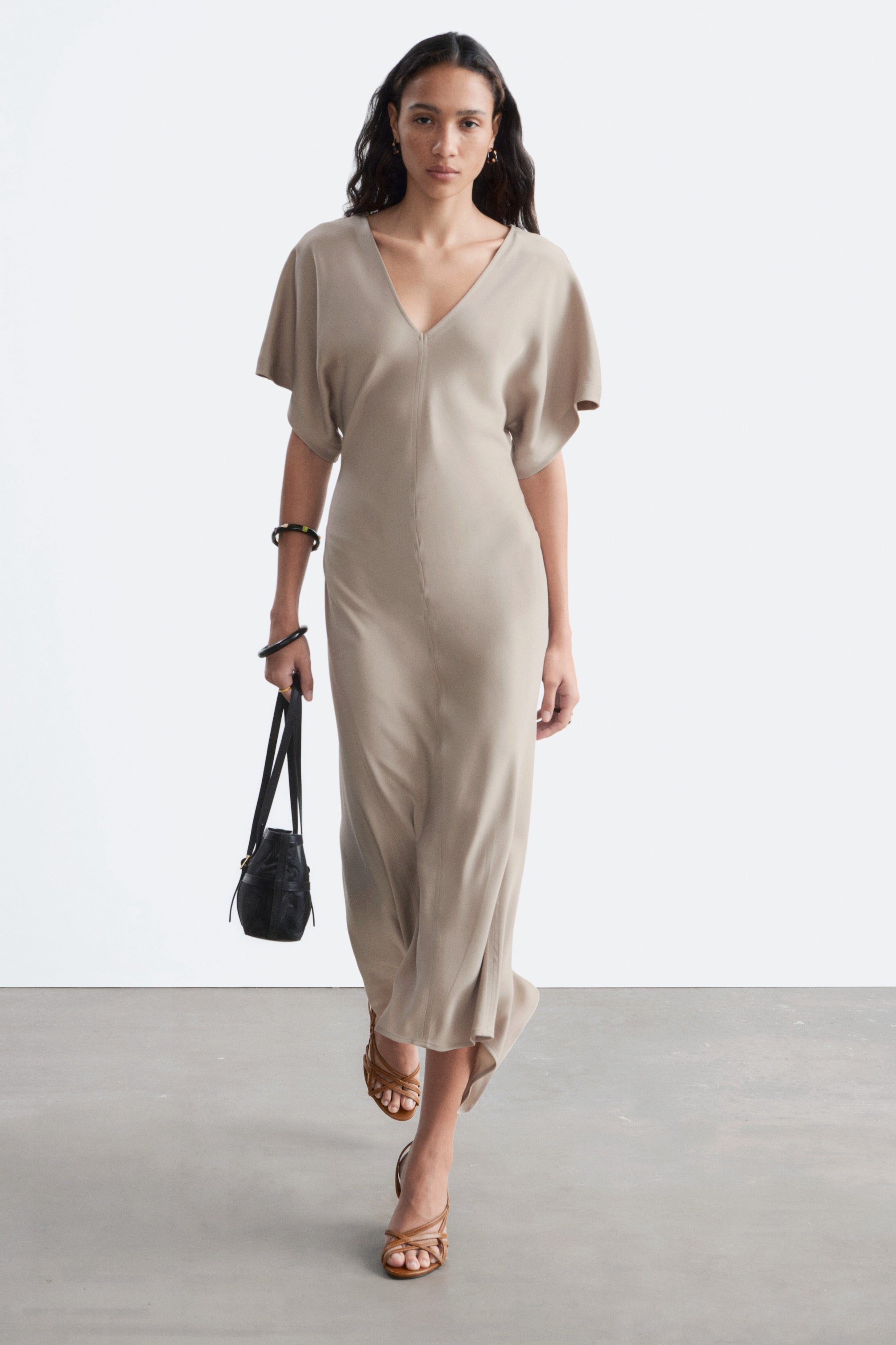 Agrandir l'image: La robe midi taupe présente un col en V, des manches courtes dolman, et une silhouette drapée et fluide avec une couture verticale sur le devant.