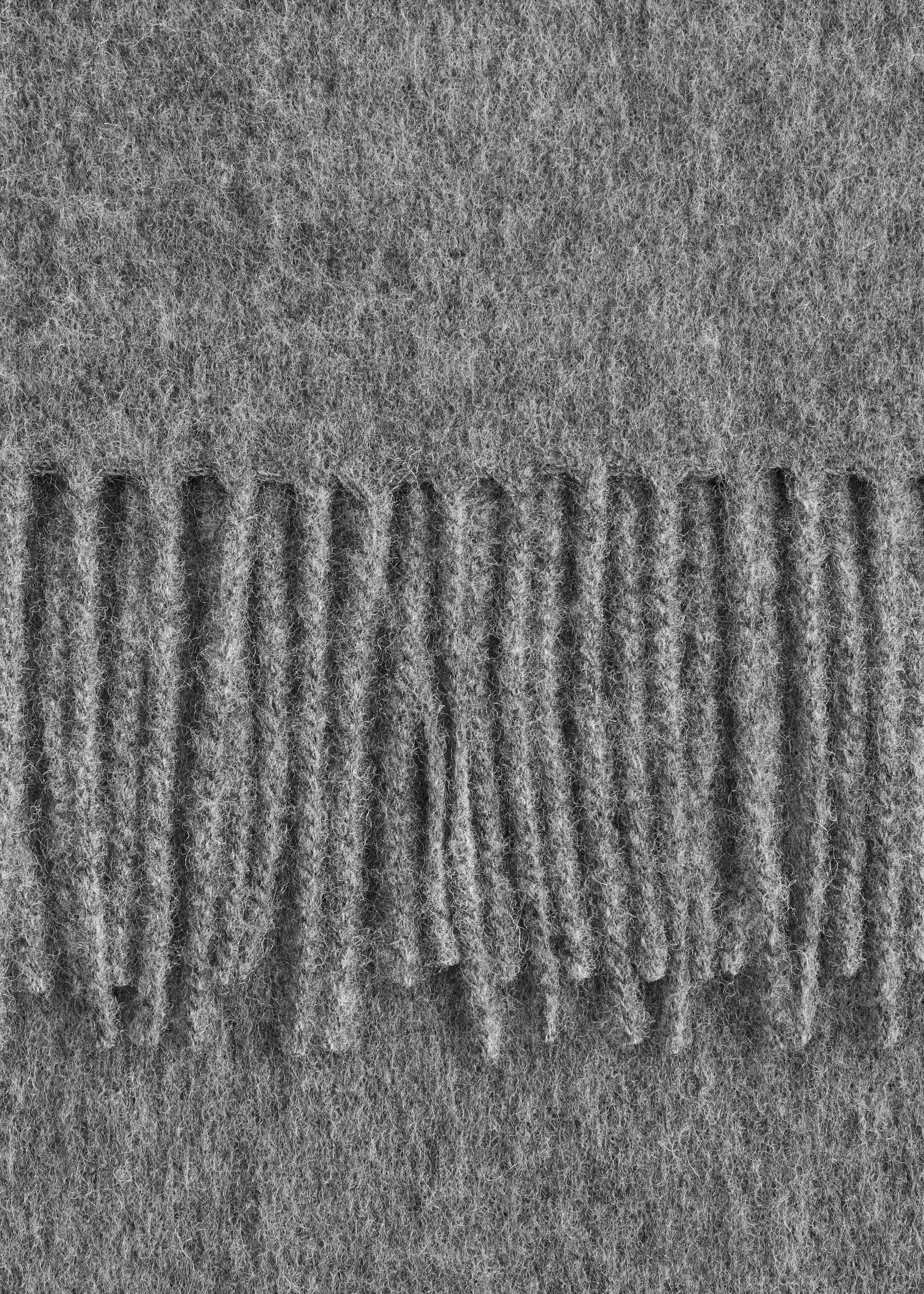 Visualizza immagine più grande: Una sezione di una grande sciarpa di lana è di un colore grigio solido e ha una consistenza morbida e sfocata. Al centro si nota una finitura con frange orizzontali, che presenta singoli fili di lana.