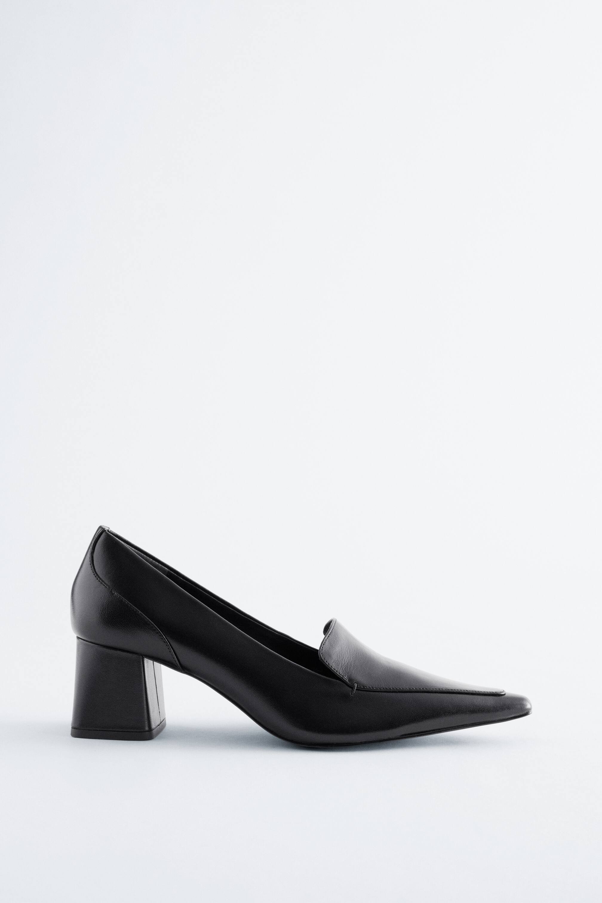 Vis større bilde: En svart loafer-pumps i skinn viser sin sideprofil, med en klassisk loafer-vamp, en spiss firkantet tå og en middels høy rektangulær blokkhæl.