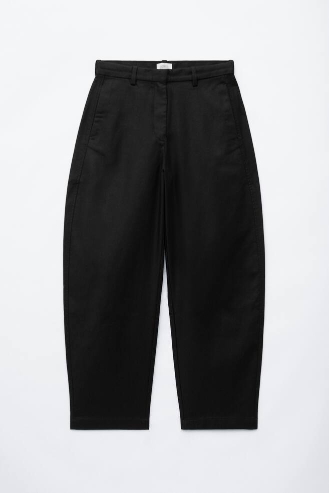 Die schwarzen Twill-Hose mit Barrel-Leg-Schnitt aus Baumwolle sind von vorne zu sehen und prÃ¤sentieren einen hochgeschnittenen Bund mit GÃ¼rtelschlaufen und Seitentaschen. Die Hose zeigt eine strukturierte Barrel-Leg-Silhouette, die sich am Oberschenkel nach auÃen wÃ¶lbt und zum Saum hin schmaler zulÃ¤uft. - 1
