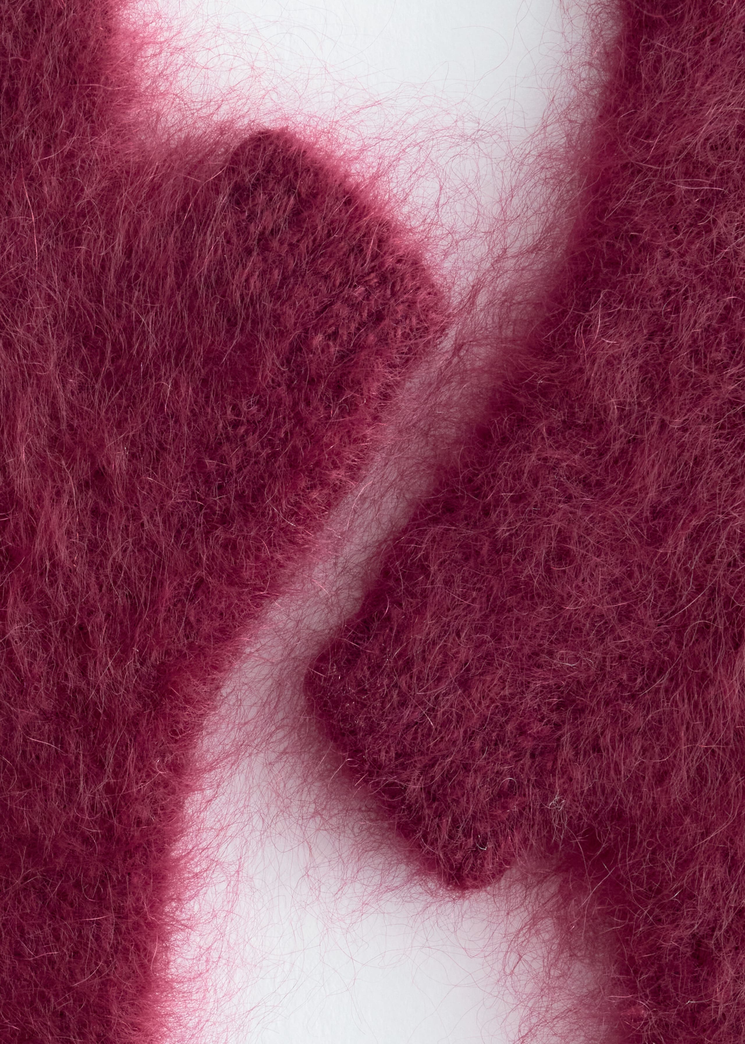A close-up view of deep magenta fingerless gloves showcases the fluffy, brushed texture of the cashmere fabric with its long, soft fibers.