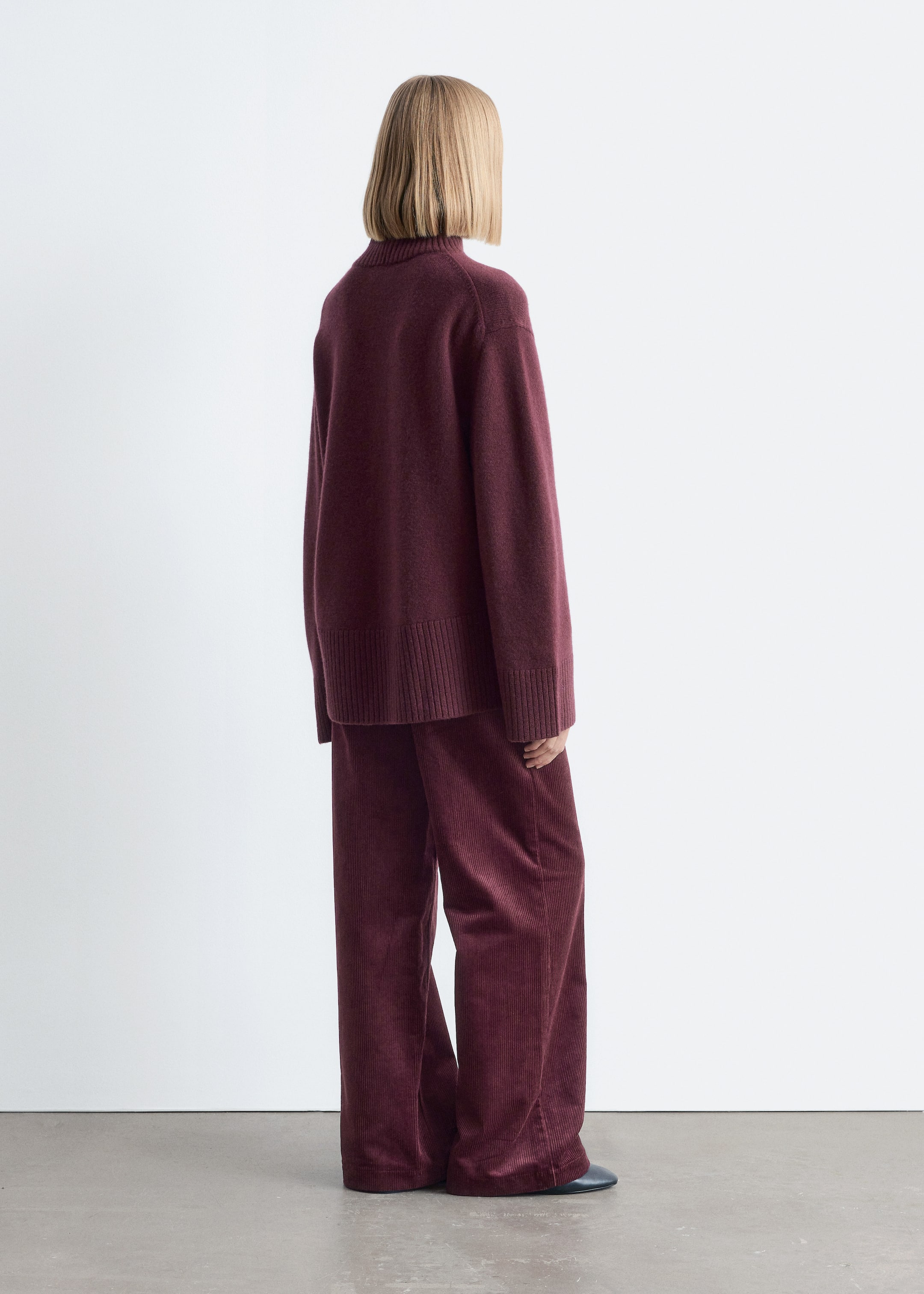 Grotere afbeelding bekijken: Een bordeaux coltrui met een oversized silhouet, geribbelde kraag, manchetten en zoom wordt gedragen door het model, die ook bijpassende wijde corduroy broek draagt.