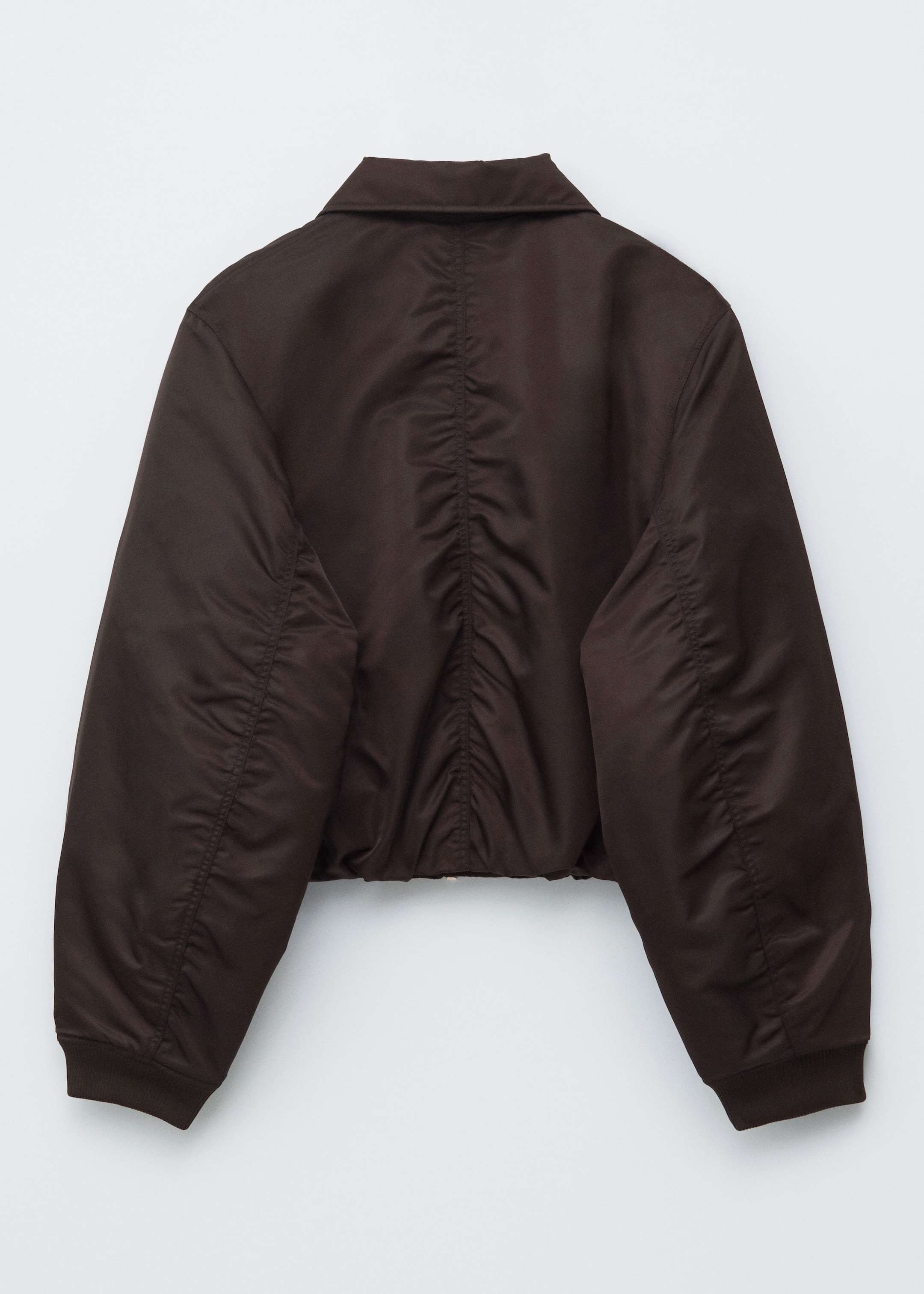 Ingrandisci l'immagine: Una giacca bomber marrone scuro è mostrata da dietro, caratterizzata da una silhouette squadrata e corta. Presenta un colletto classico, un'arricciatura prominente lungo il centro della schiena e le cuciture delle braccia, e polsini e orlo a coste.