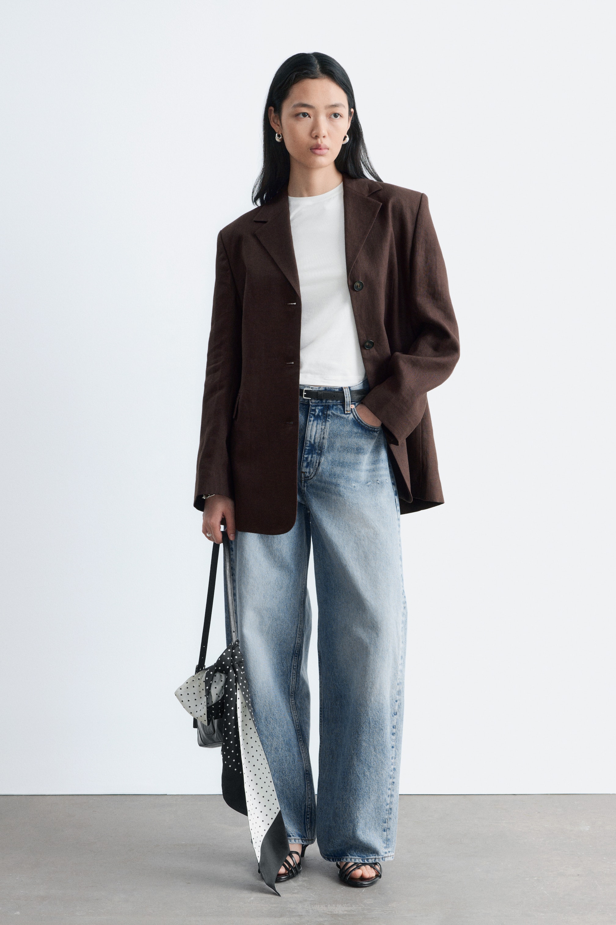 Ver imagen más grande: Se lleva un blazer marrón de talla grande, con hombros estructurados, solapas de muesca y un cierre frontal de dos botones. Está combinado con una camiseta blanca y vaqueros de lavado claro.