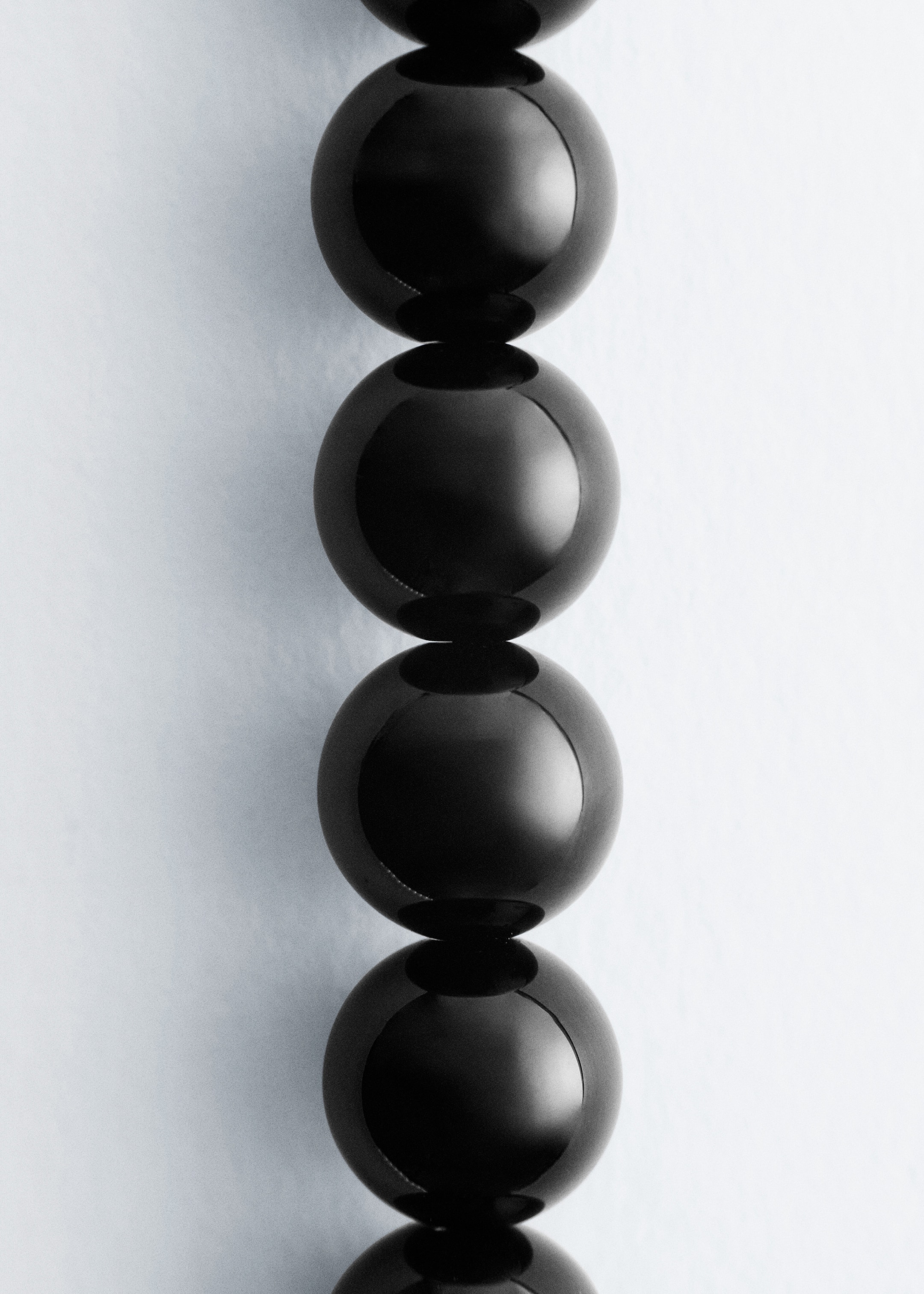 Visualizza immagine più grande: Un segmento di una collana mostra perle di pietra nere e sferiche, le loro superfici lucide riflettono la luce.