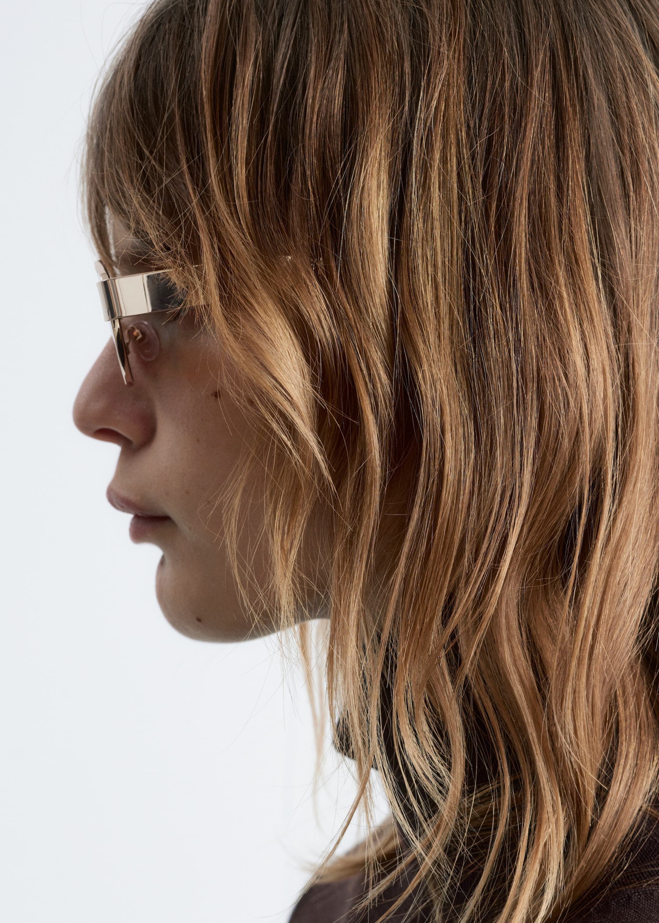 Agrandir l'image: Une paire de lunettes sans monture est portée, vue de profil, avec une large barre supérieure en métal poli qui s'étend sur le pont et les branches, avec des verres transparents visibles en dessous.