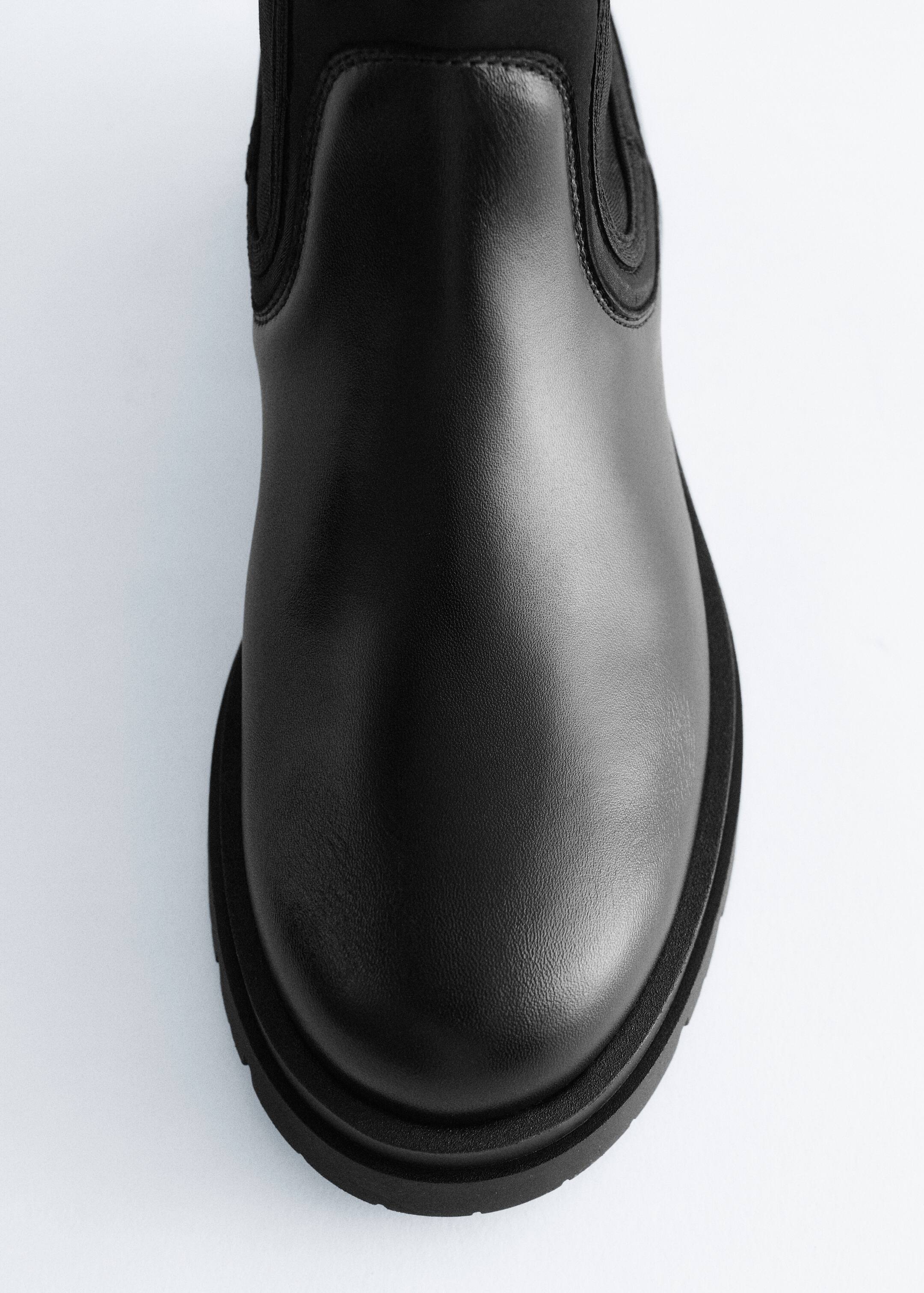Grösseres Bild ansehen: Ein schwarzer Chelsea-Boot wird aus der Vorderansicht präsentiert, zeigt sein glattes Leder-Vorderblatt und die Zehenpartie, elastische Seiteneinsätze und einen matten Stoffschaft, alles auf einer klobigen, profilierten Sohle.