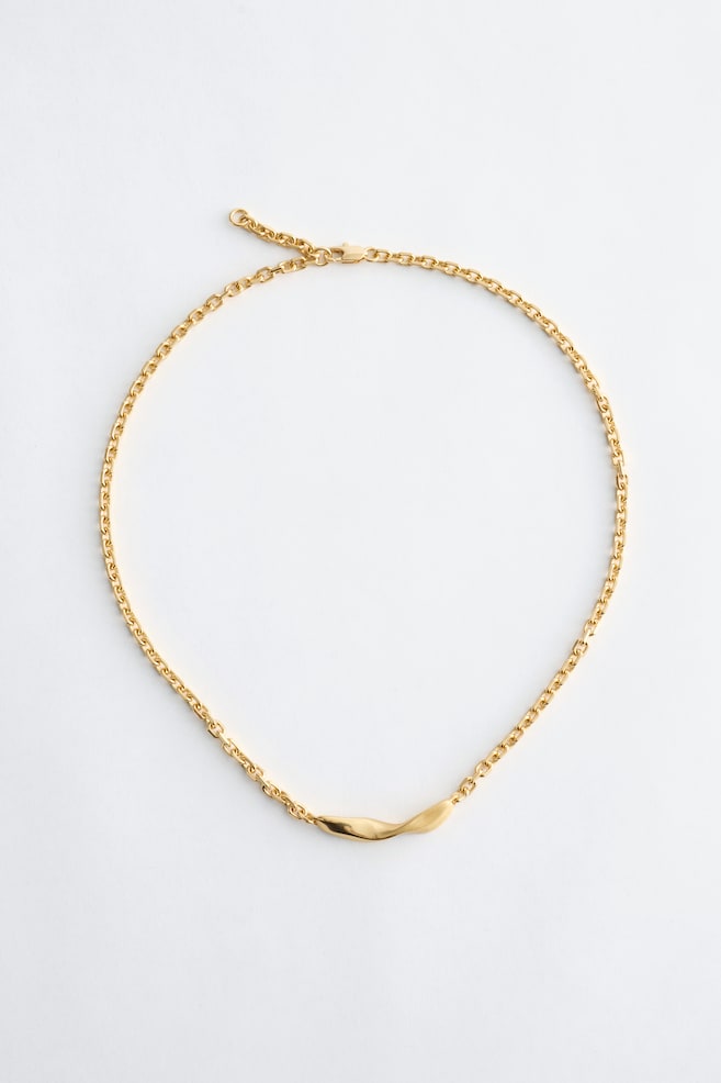 Un collier chaîne de couleur dorée est posé à plat, mettant en valeur un détail de barre torsadée en son centre, avec un fermoir mousqueton et une chaîne d'extension positionnés en haut. - 1
