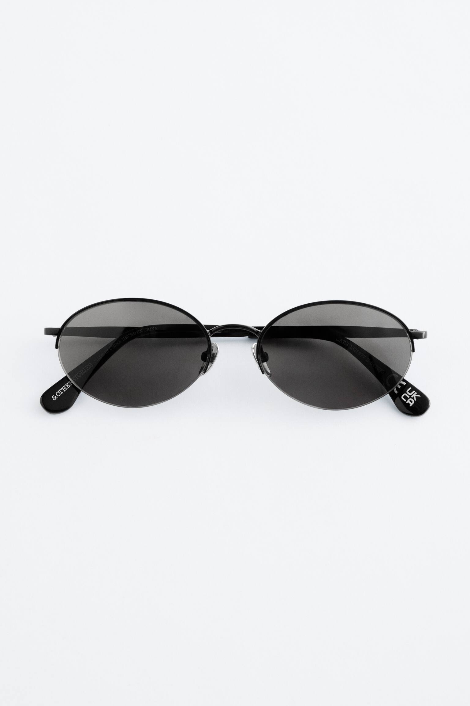 Las gafas de sol con montura de alambre están mostrando su vista frontal. Presentan lentes redondos de color negro con varillas delgadas de acero negro y almohadillas nasales ajustables. - 1
