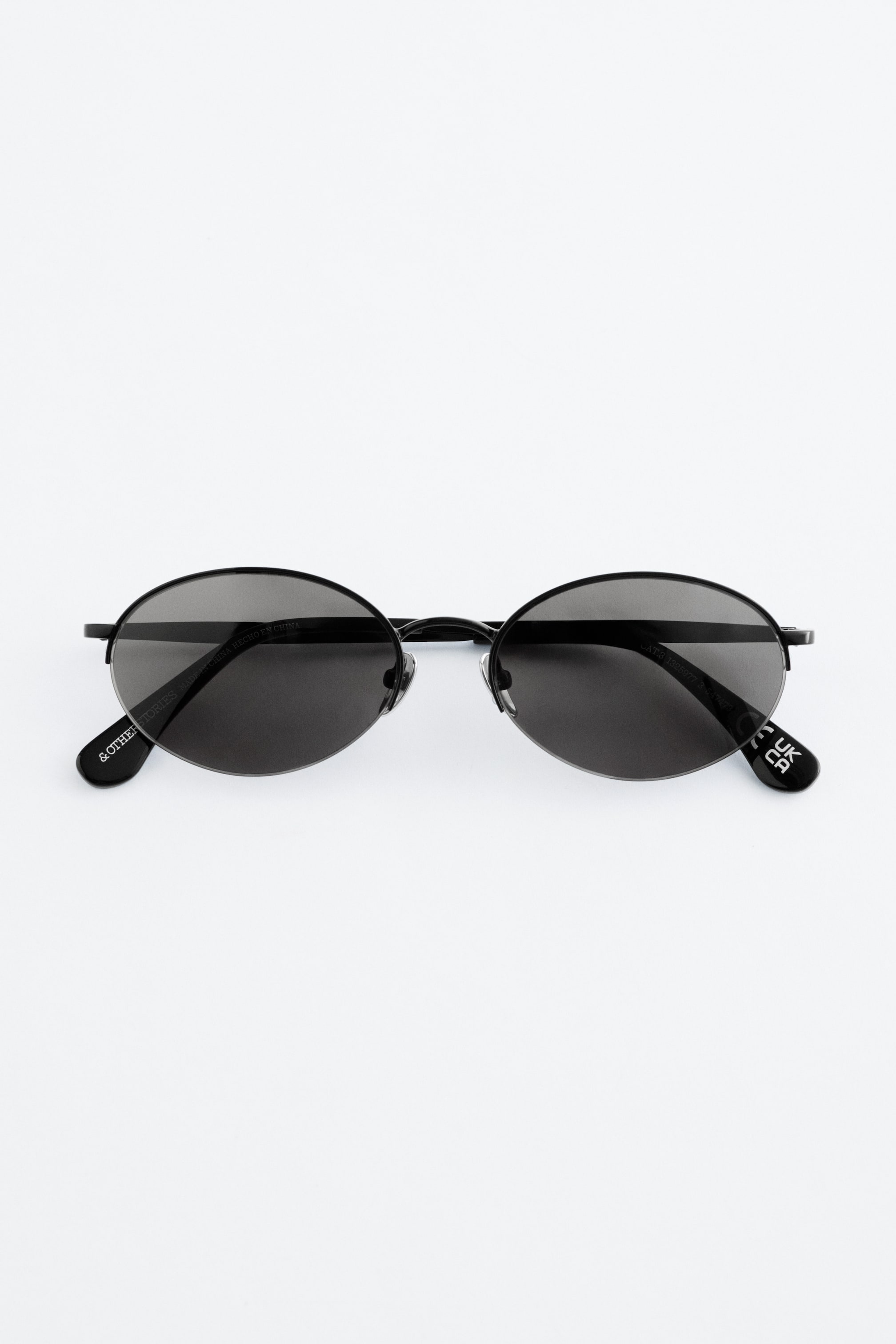 Agrandir l'image: Les lunettes de soleil à monture filaire sont présentées de face. Elles arborent des verres ronds et noirs avec des branches en acier noir fin et des plaquettes de nez ajustables.