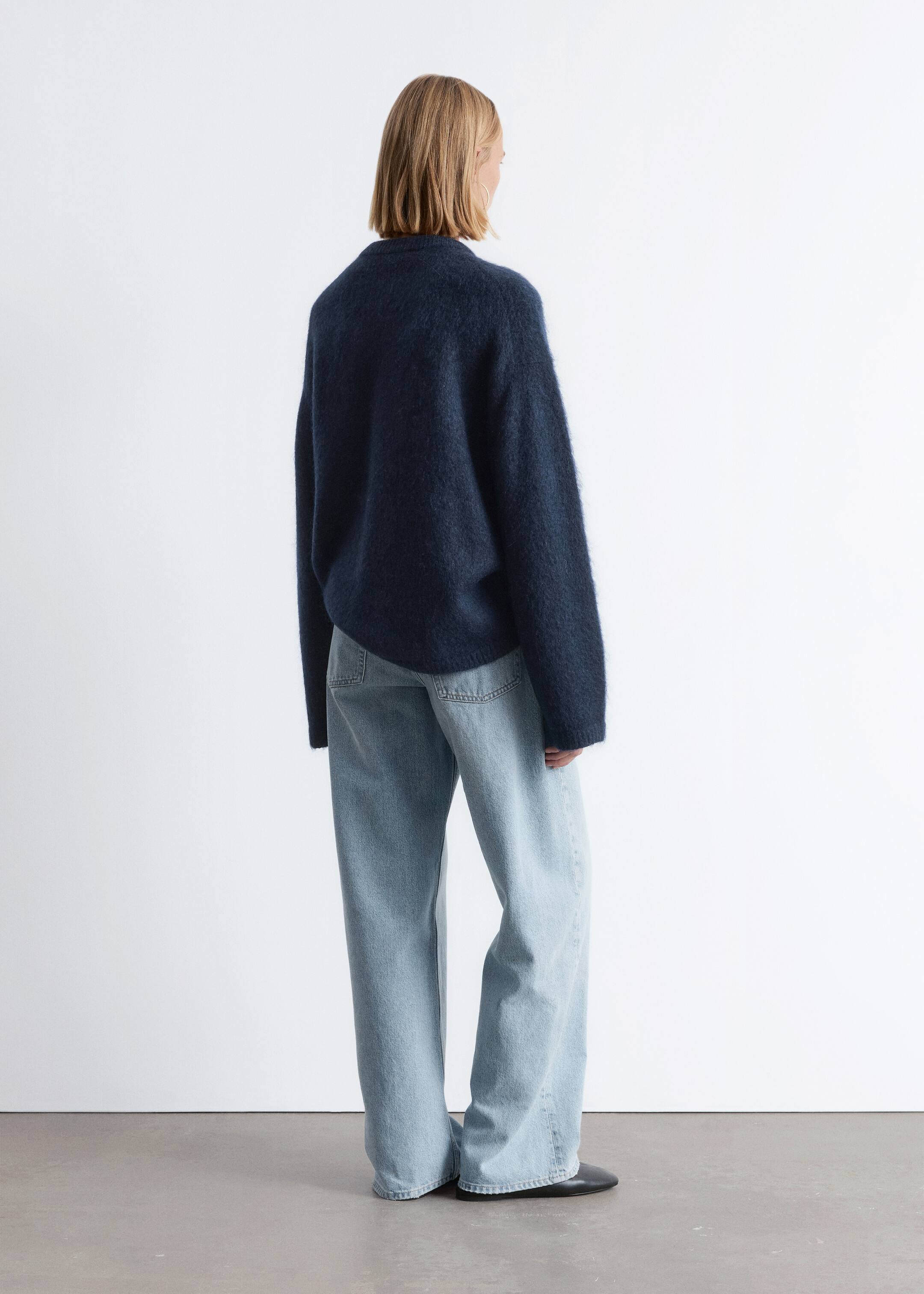 Agrandir l'image: Un pull bleu foncé, duveteux avec une coupe décontractée et des manches longues est montré de dos, légèrement incliné. Il est porté sur un jean bleu clair à jambes larges, qui présente des poches arrière visibles et une coupe décontractée pleine longueur.