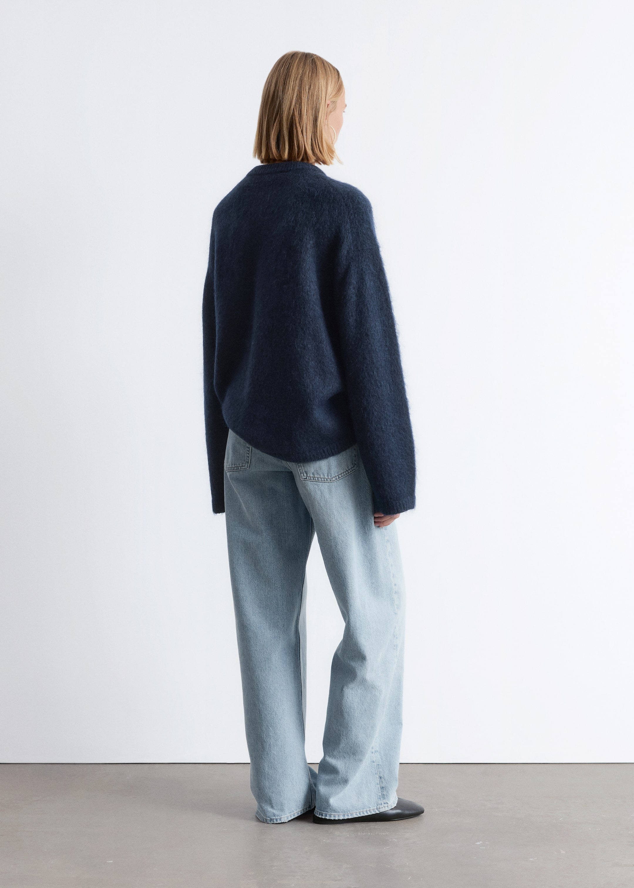 Visa större bild: En mörkblå, luddig tröja med avslappnad passform och långa ärmar visas bakifrån, något vinklad. Den bärs över ljusblå, vida jeans, som har synliga bakfickor och en fullängds, avslappnad skärning.
