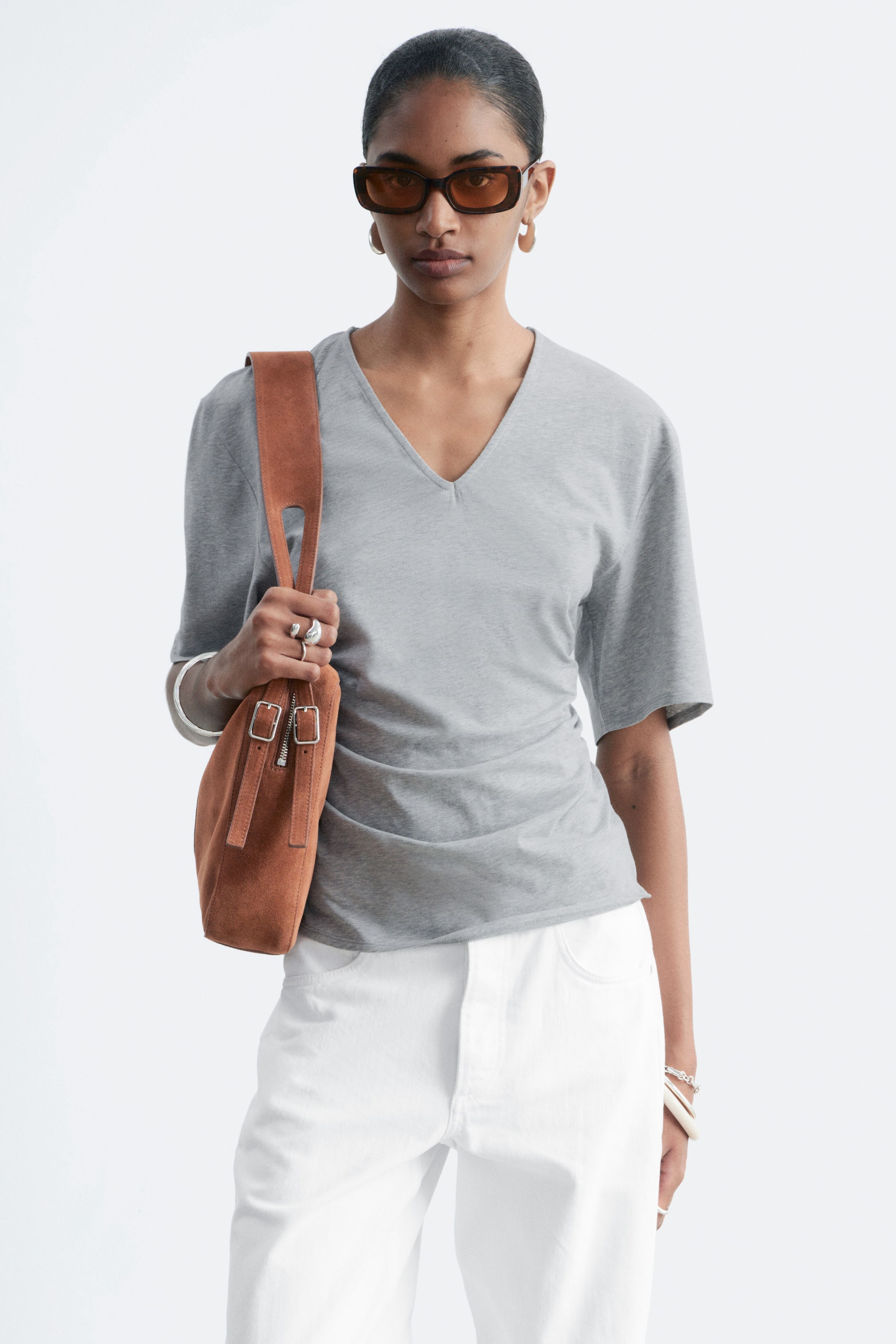 Grösseres Bild ansehen: Ein graues V-Ausschnitt-Top mit ellbogenlangen Ärmeln, das sanft fällt und auf der linken Seite mit Raffungen versehen ist.