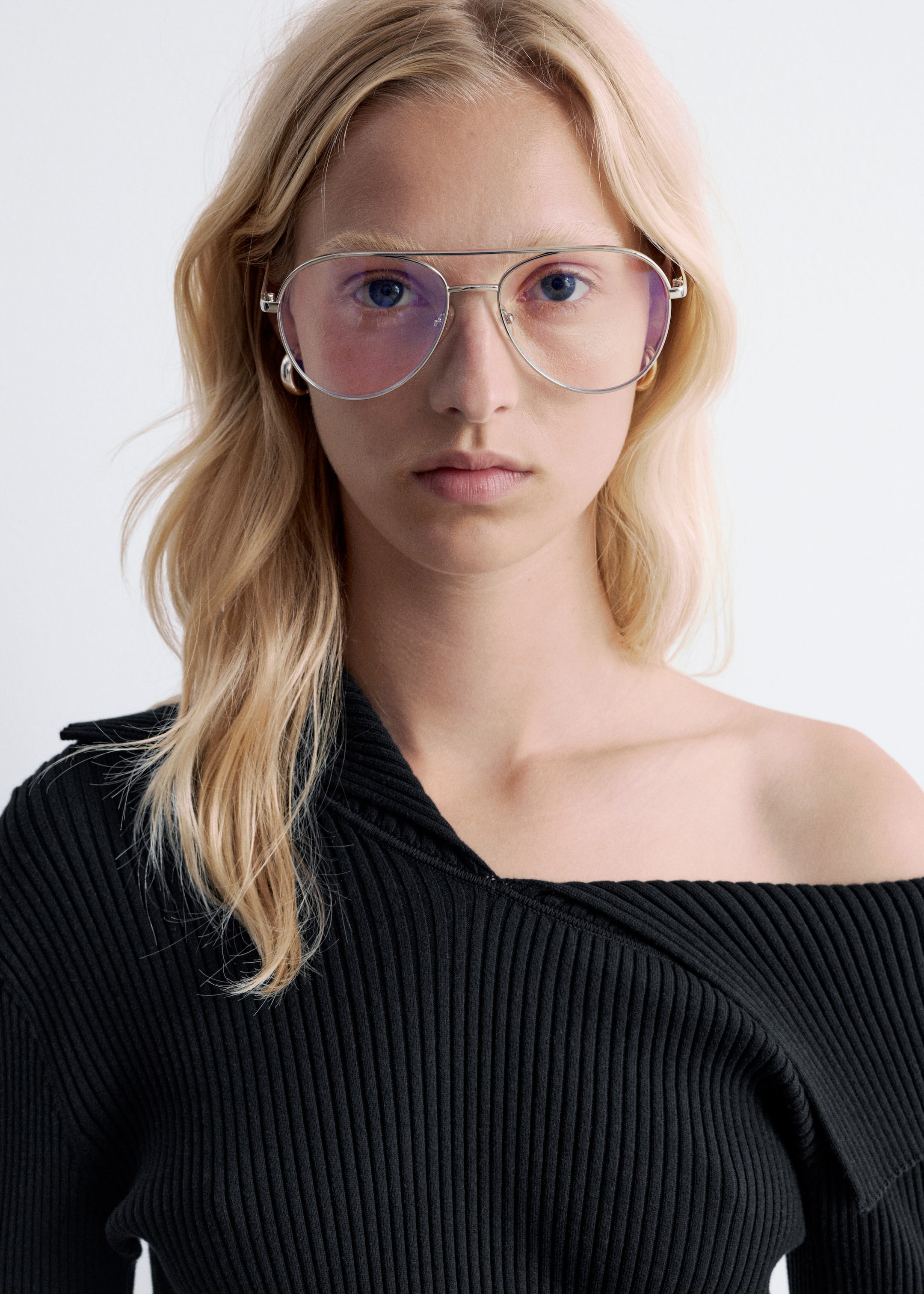 Agrandir l'image: Des lunettes de soleil aviateur argentées avec des verres teintés roses sont portées par le mannequin, qui porte également un haut noir à manches longues côtelé avec un décolleté asymétrique et un col marin replié pour un look épaules dénudées.