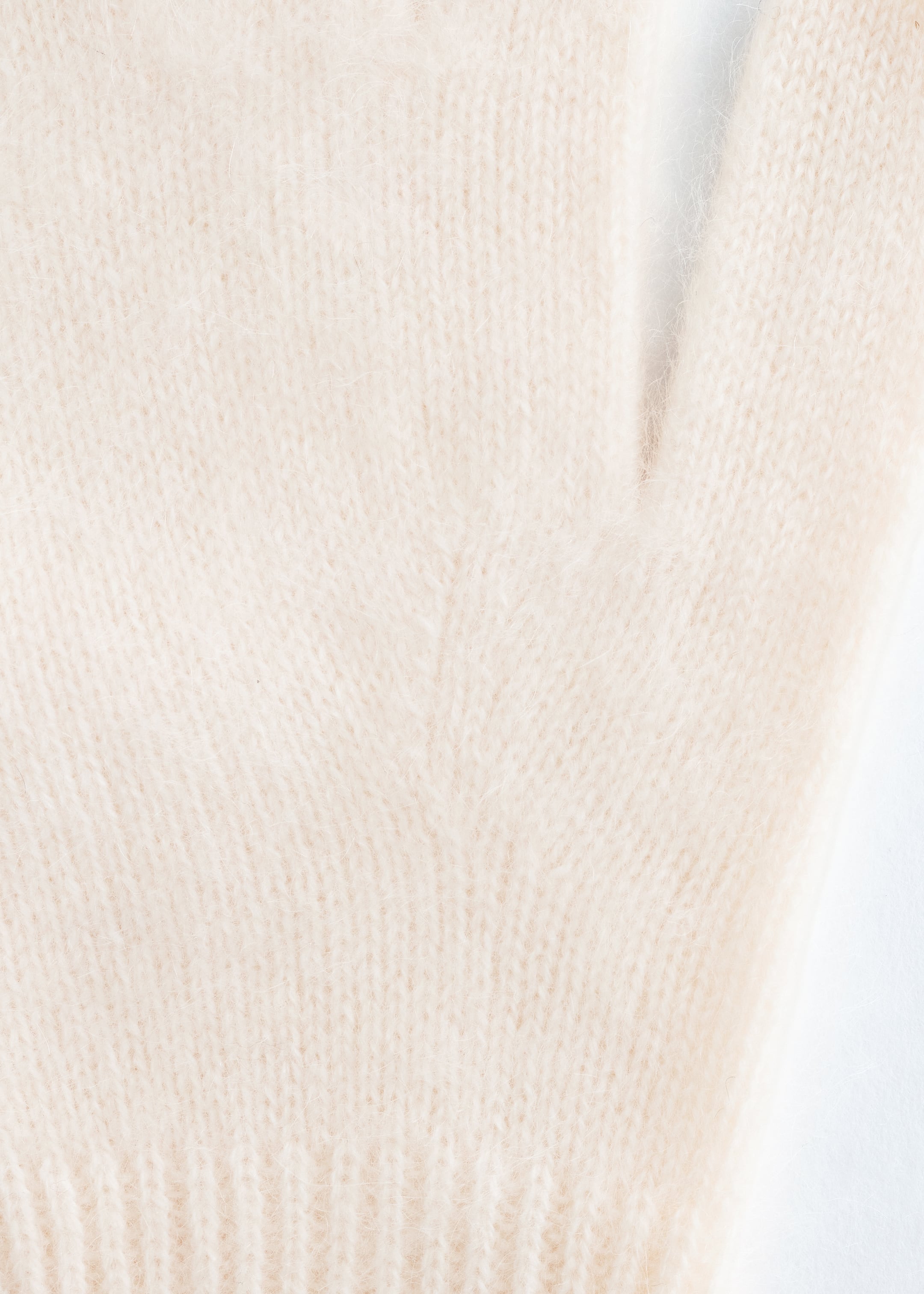View larger image: A pale cream knitted brushed cashmere glove is laid flat, showcasing its soft, fuzzy texture. The glove is featuring a ribbed cuff at the bottom, and its thumb portion is extending to the LEFT.