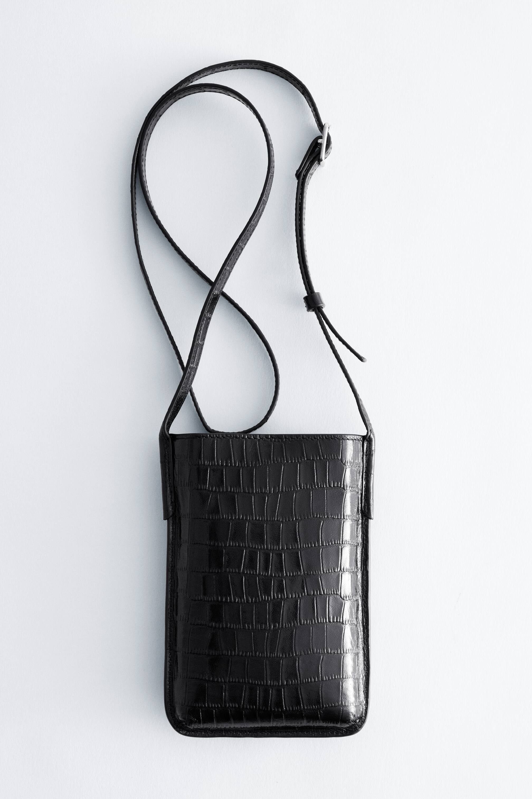 Grotere afbeelding bekijken: Een kleine, langwerpige zwarte telefoontas met een croco-embossed textuur wordt van voren getoond en laat de rechthoekige vorm met afgeronde onderste hoeken zien. De tas is voorzien van een dunne, verstelbare bijpassende schouderriem met een metalen gesp in zilverkleur.