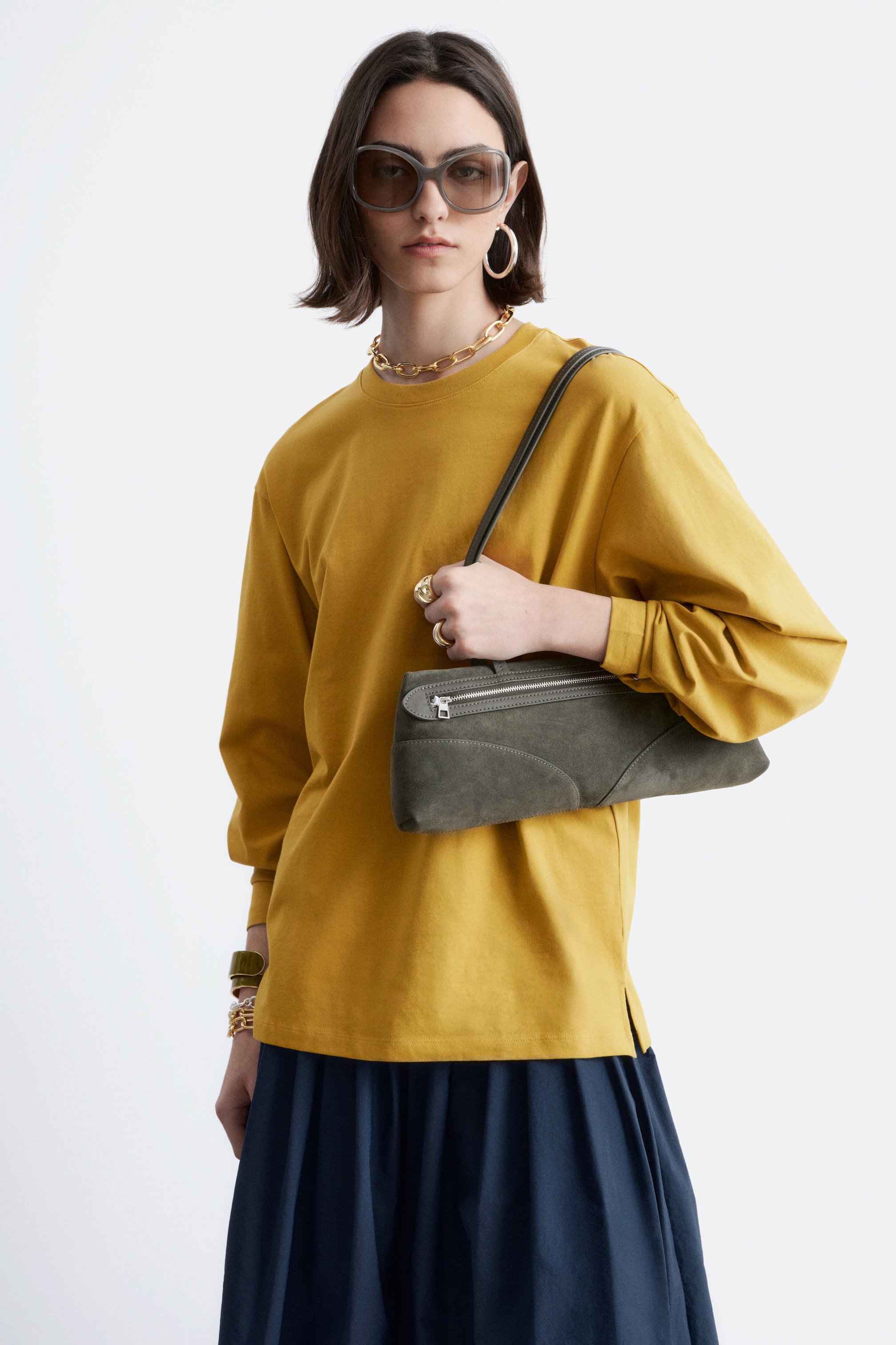 Nagyobb kép megtekintése: Egy mustársárga, hosszú ujjú felső látható enyhén elölről-jobbról szögből, kerek nyakkivágással és laza, bő szabással. Egyenes szegélye a bal oldalon egy kis oldalsliccel mutatkozik, és a hosszú ujjak lazán esnek a csuklókig.