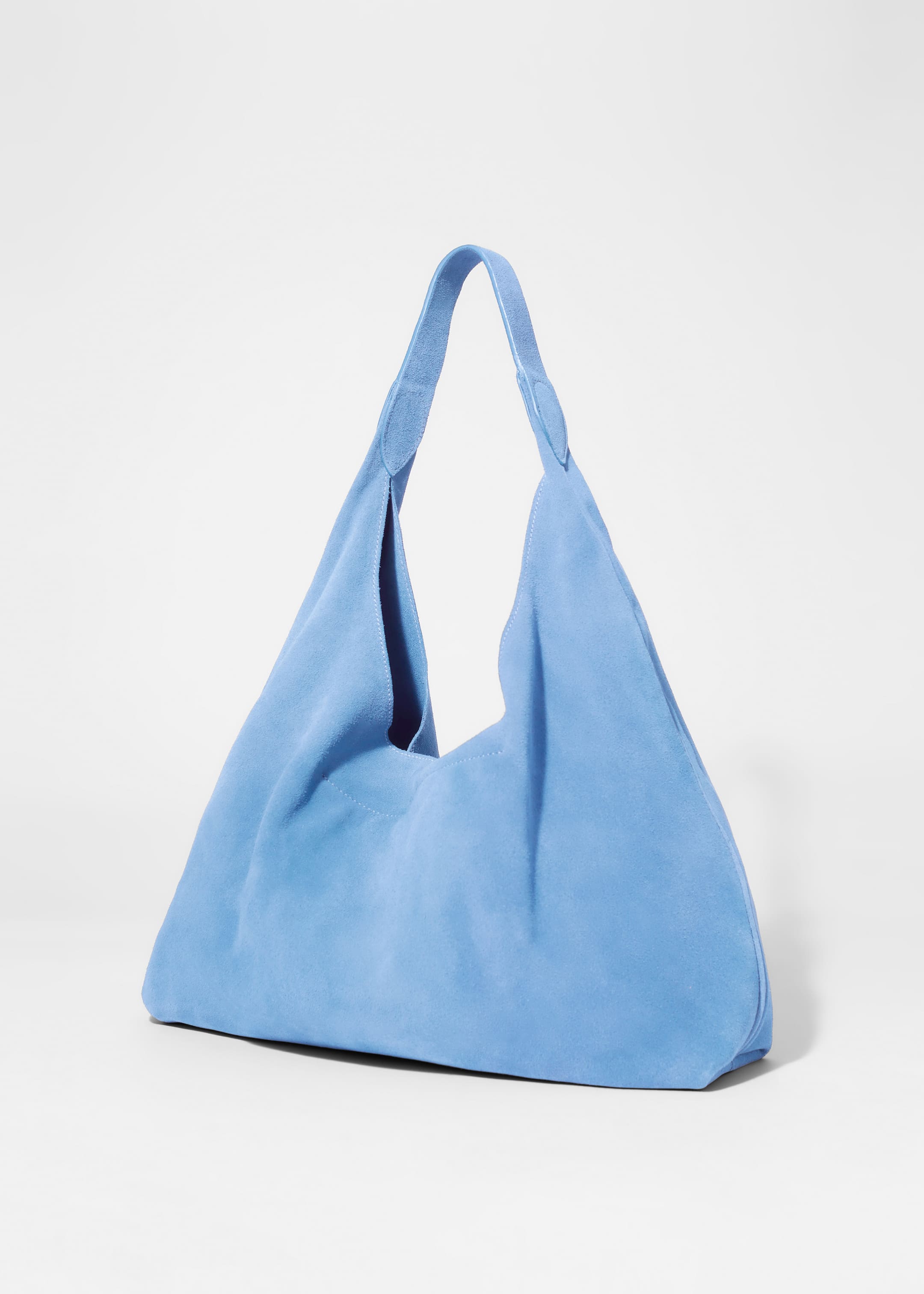 Ver imagen más grande: Un bolso de mano de gamuza azul con acabado mate está mostrando su estructura suave y una sola correa ancha. Está destacando una costura decorativa que corre verticalmente por el centro de su lado visible, y la correa se une al bolso utilizando pestañas de gamuza ovaladas.