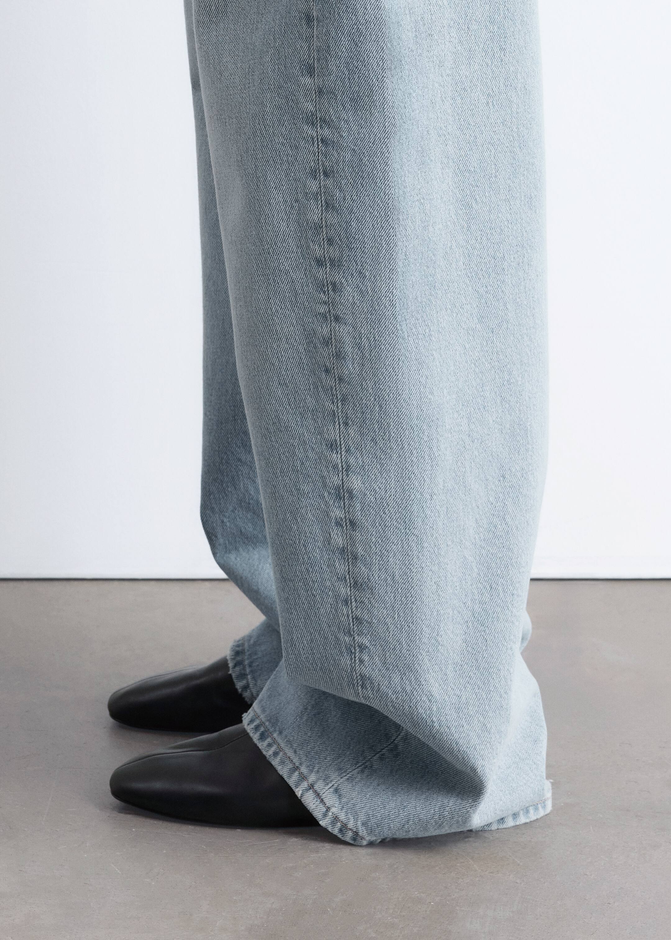 View larger image: Light blue, wide-leg jeans are pooling over black, pointed-toe shoes. The denim fabric is displaying a subtle washed effect, and vertical seams are running down the legs.