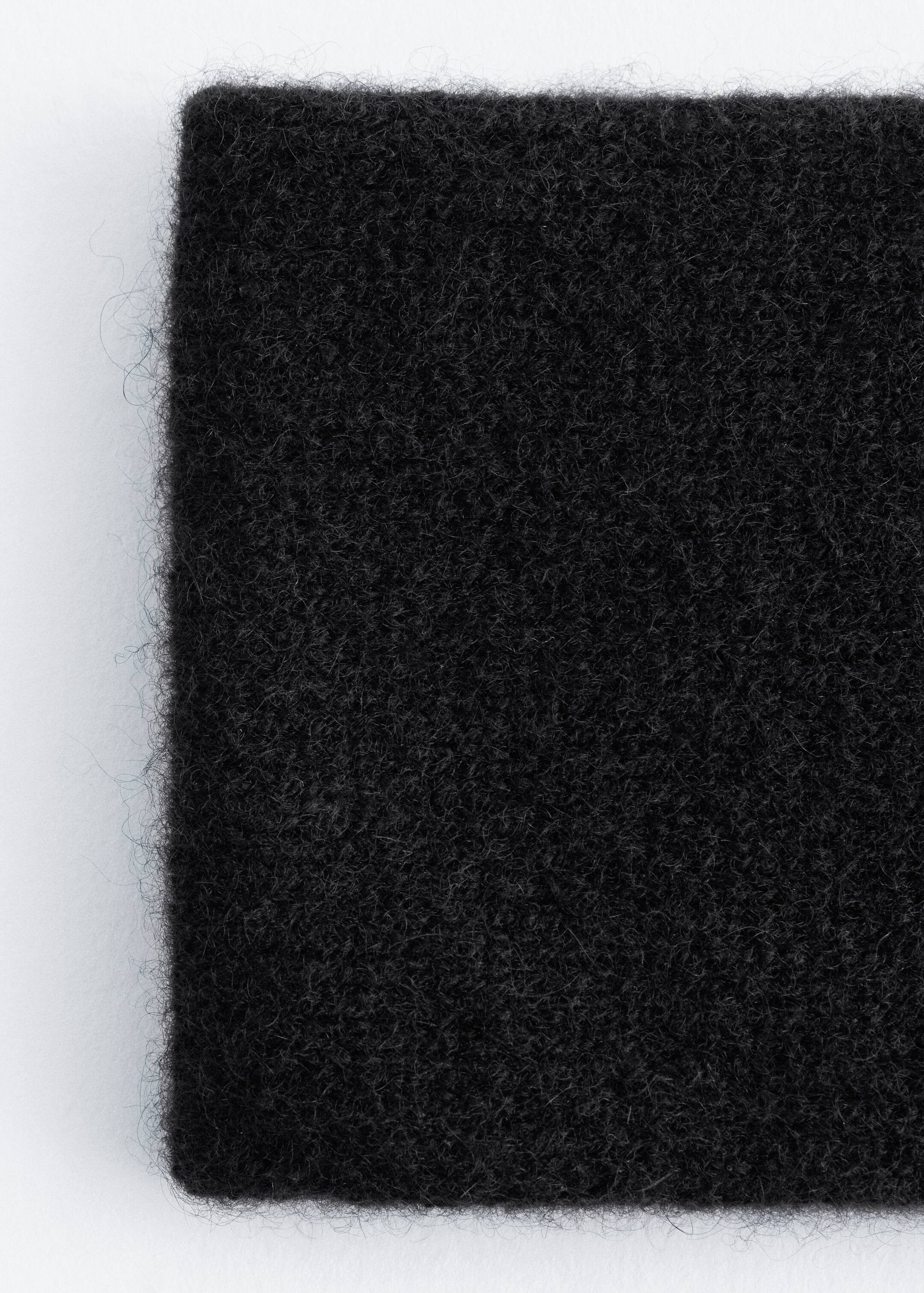 Ver imagem maior: Uma bandolete de caxemira preta está a ser mostrada em close-up, destacando a sua textura suave, densa e felpuda com fibras visíveis.