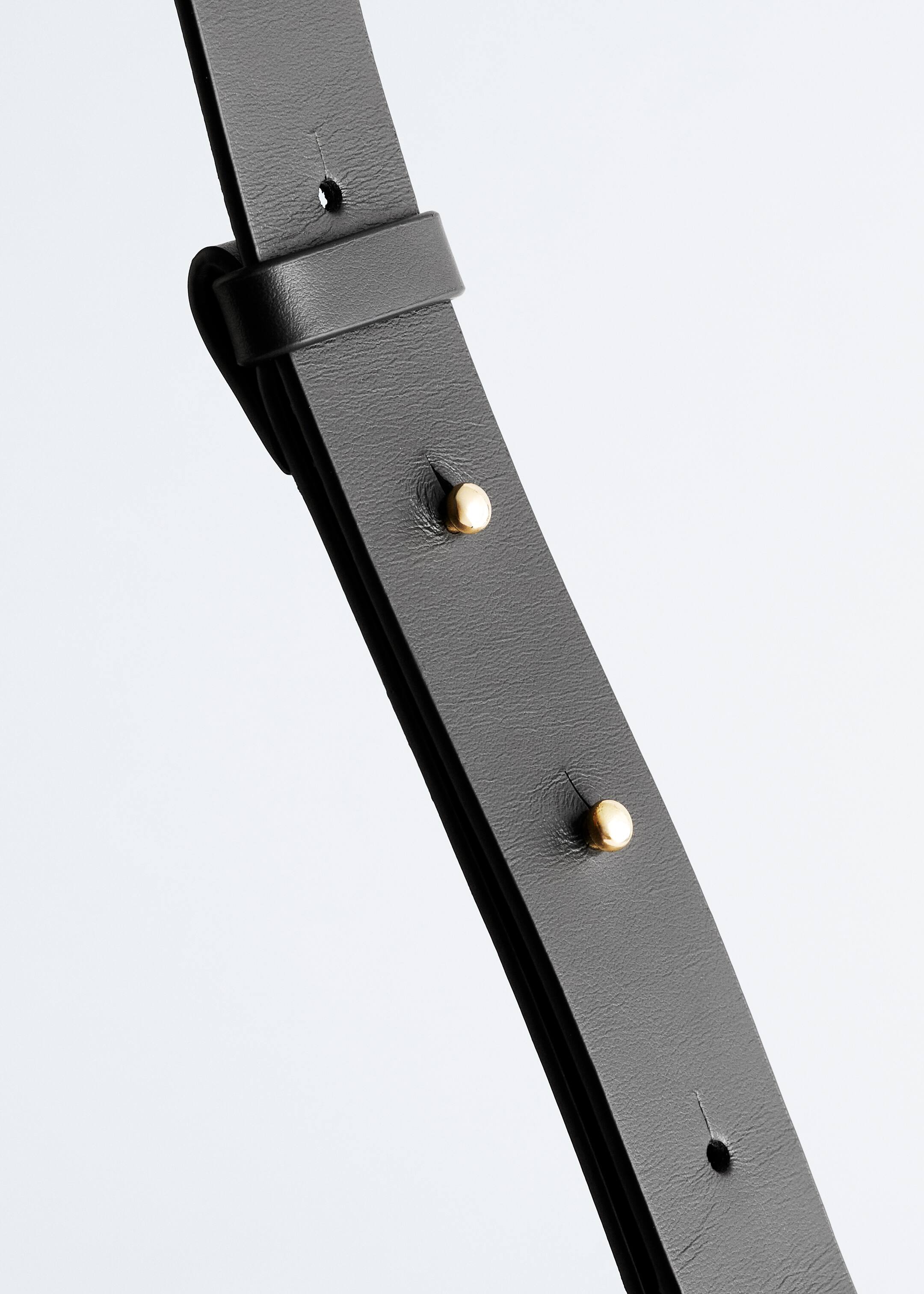 Grotere afbeelding bekijken: Een zwarte leren verstelbare schouderriem is voorzien van goudkleurige studs en een leren lus om de riem op zijn plaats te houden, met een zichtbaar verstelgat.