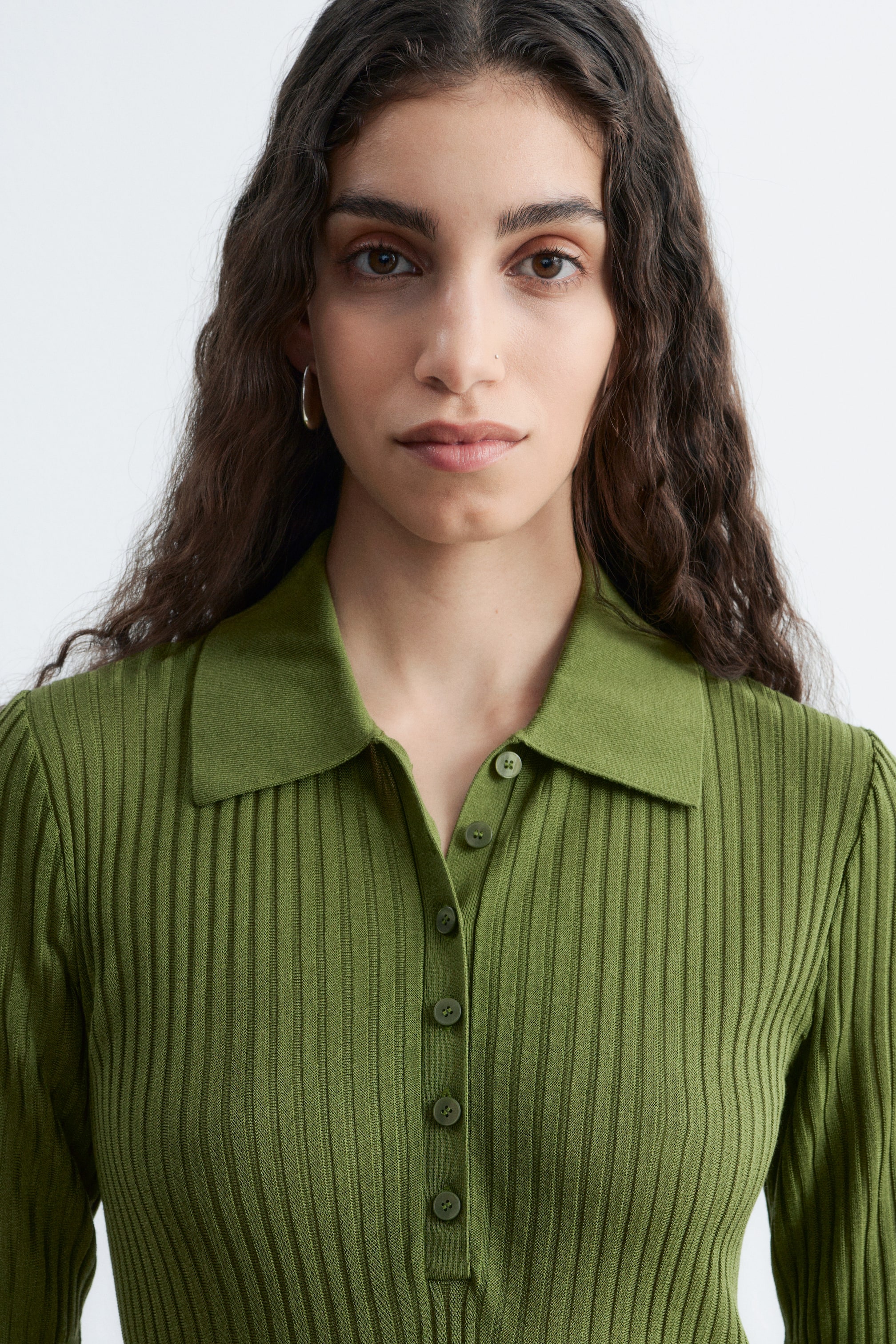Visualizza immagine più grande: Un top polo a maglia a coste di colore verde oliva presenta un colletto a punta e un'abbottonatura con bottoni coordinati, mettendo in risalto una texture a coste verticali lungo il corpo e le maniche lunghe.