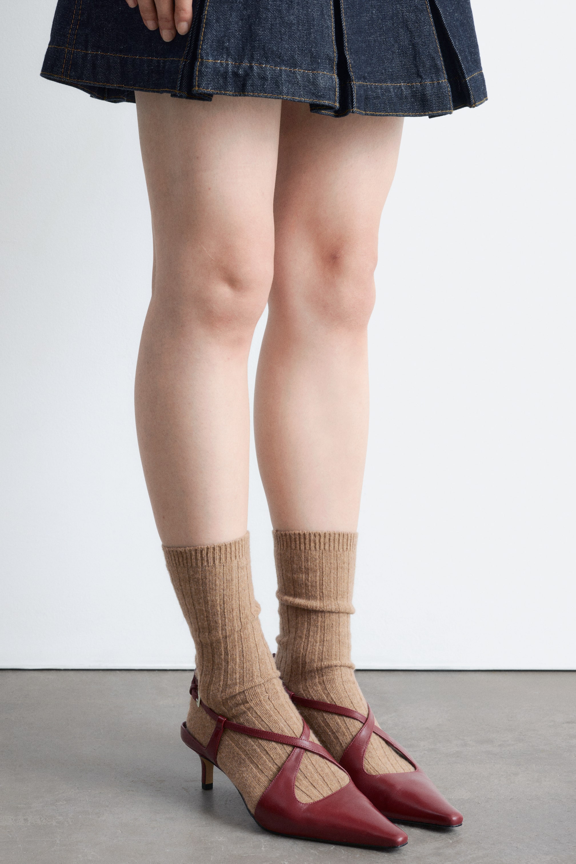 Größeres Bild ansehen: Burgunderrote Slingback-Kätzchenabsätze aus Leder mit spitzer Zehenpartie und überkreuzten Riemen am Vorderfuß werden vom Model mit hellbraunen gerippten Socken getragen.