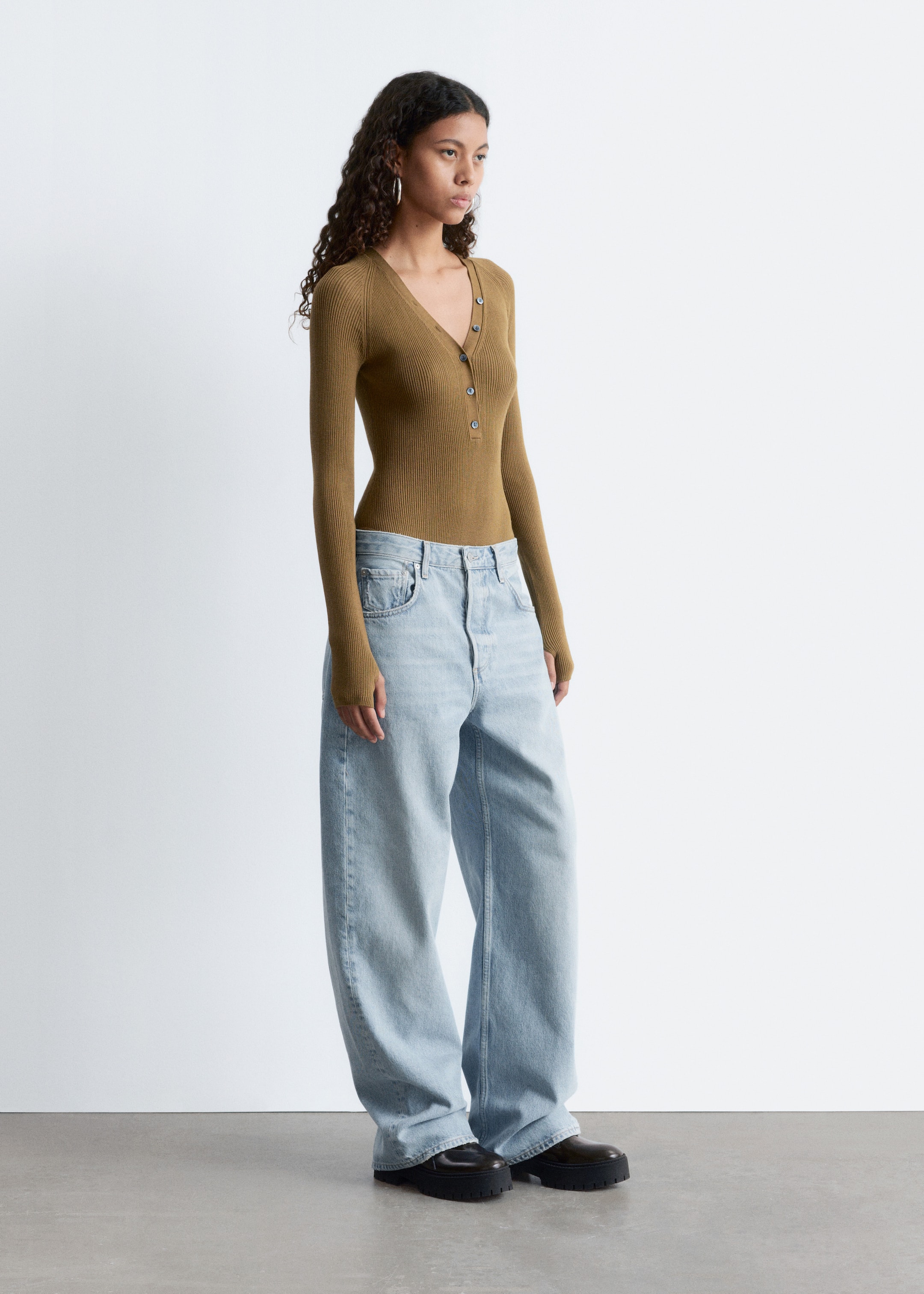 View larger image: A slim-fit, olive brown ribbed knit top is presenting a V-neckline with a five-button henley placket from a slight side angle. It is featuring long sleeves and is shown tucked into light wash jeans.