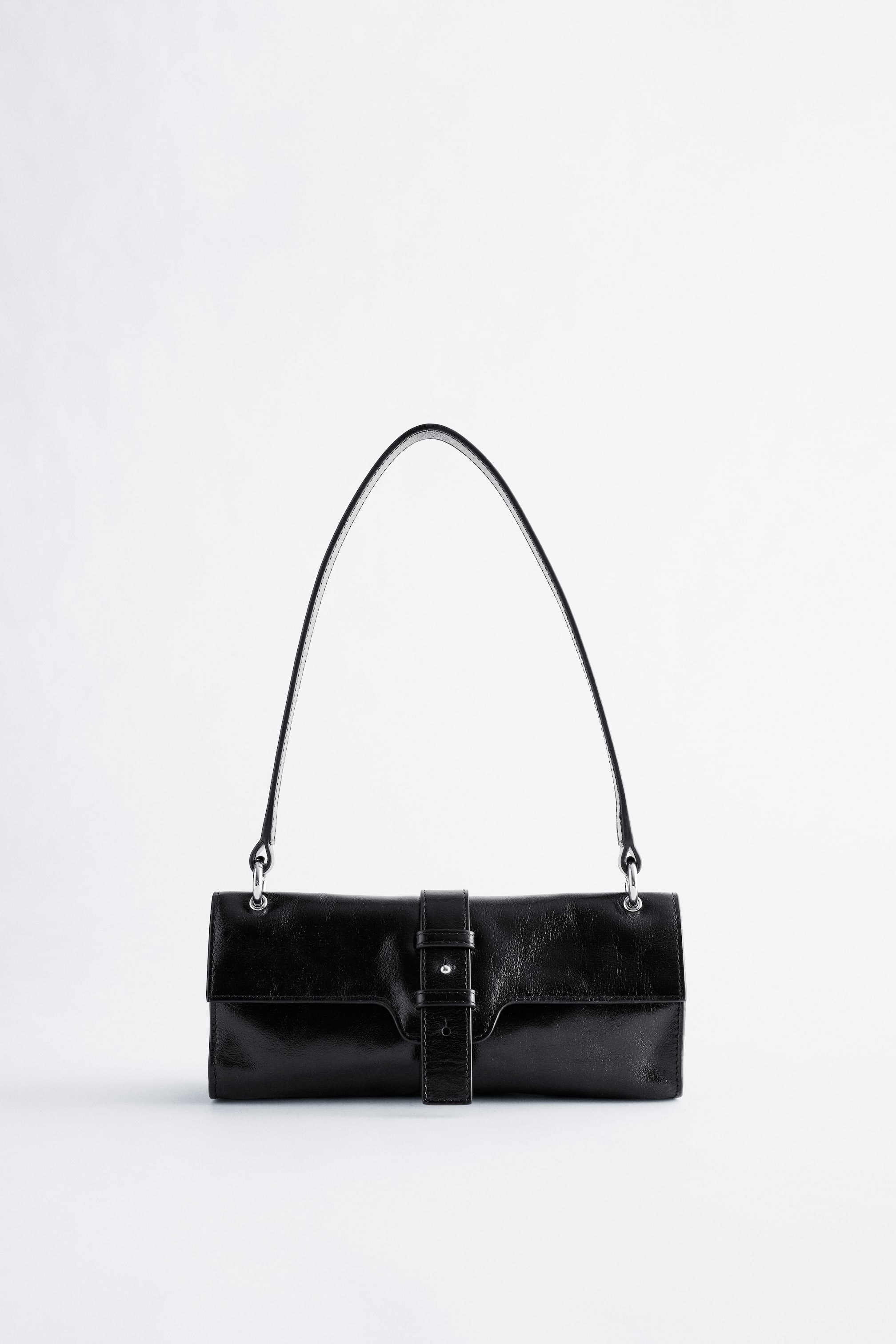 Größeres Bild ansehen: Eine schwarze Lederschultertasche zeigt ihre Vorderseite, die einen länglichen, rechteckigen Körper mit einer Klappenverschluss aufweist, der durch einen zentralen Riemen und einen silberfarbenen Nieten gesichert ist. Ein schlanker, einzelner schwarzer Schulterriemen ist mit silberfarbenen Ringen an der Oberseite der Tasche befestigt.