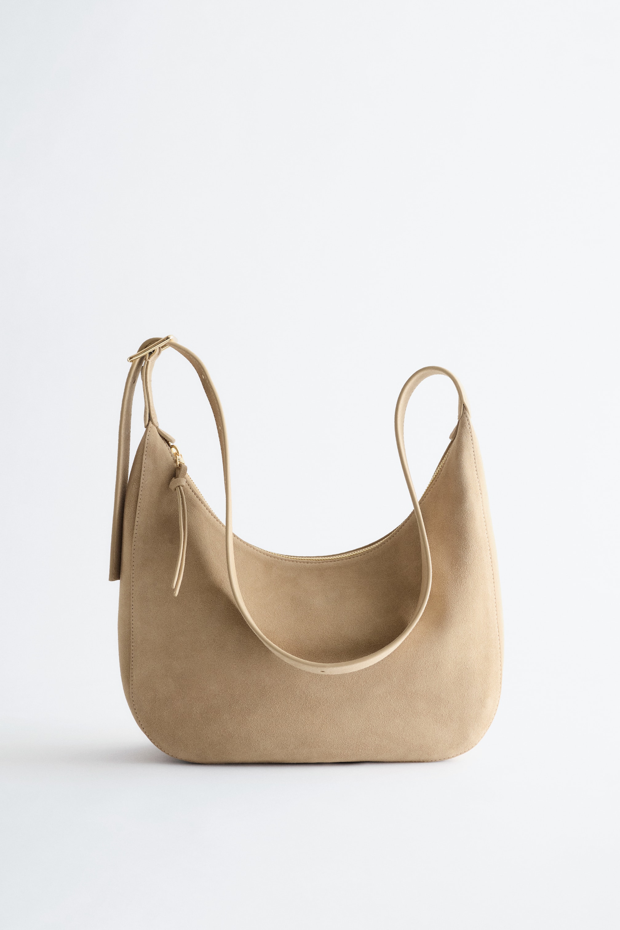 Größeres Bild anzeigen: Eine hellbraune Hobo-Tasche mit Wildlederstruktur präsentiert sich von vorne und zeichnet sich durch eine geschwungene, lässige Silhouette aus. Sie verfügt über einen langen, verstellbaren Schulterriemen mit einer goldfarbenen Schnalle und einem goldfarbenen Reißverschluss oben, der mit einem kleinen Zuglaschen-Akzent versehen ist.