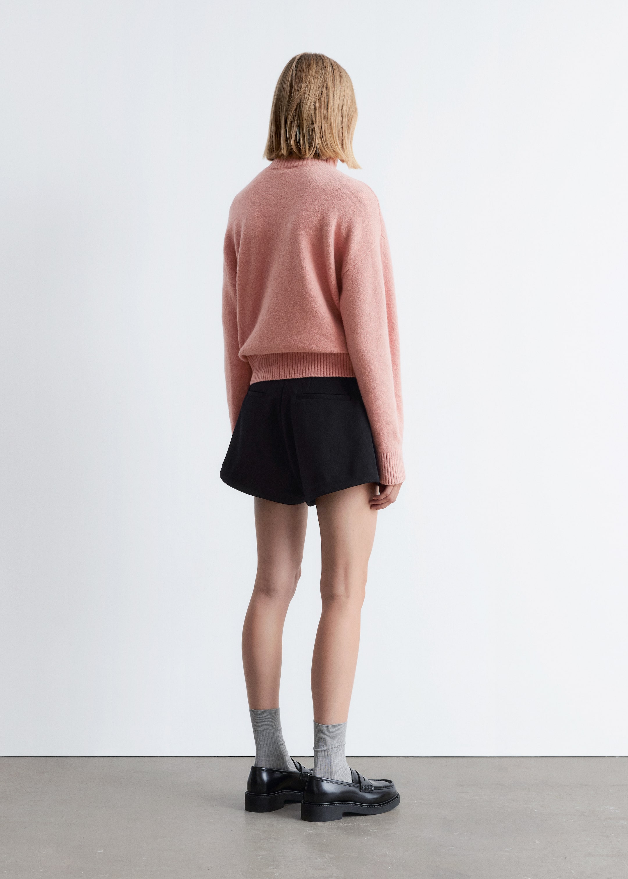 Größeres Bild anzeigen: Ein rosa Pullover und schwarze Shorts werden von hinten präsentiert. Der rosa Pullover zeigt eine entspannte Passform mit einer flauschigen Textur, langen Ärmeln und einem gerippten Saum, während die schwarzen Shorts eine strukturierte, ausgestellte Silhouette aufweisen.