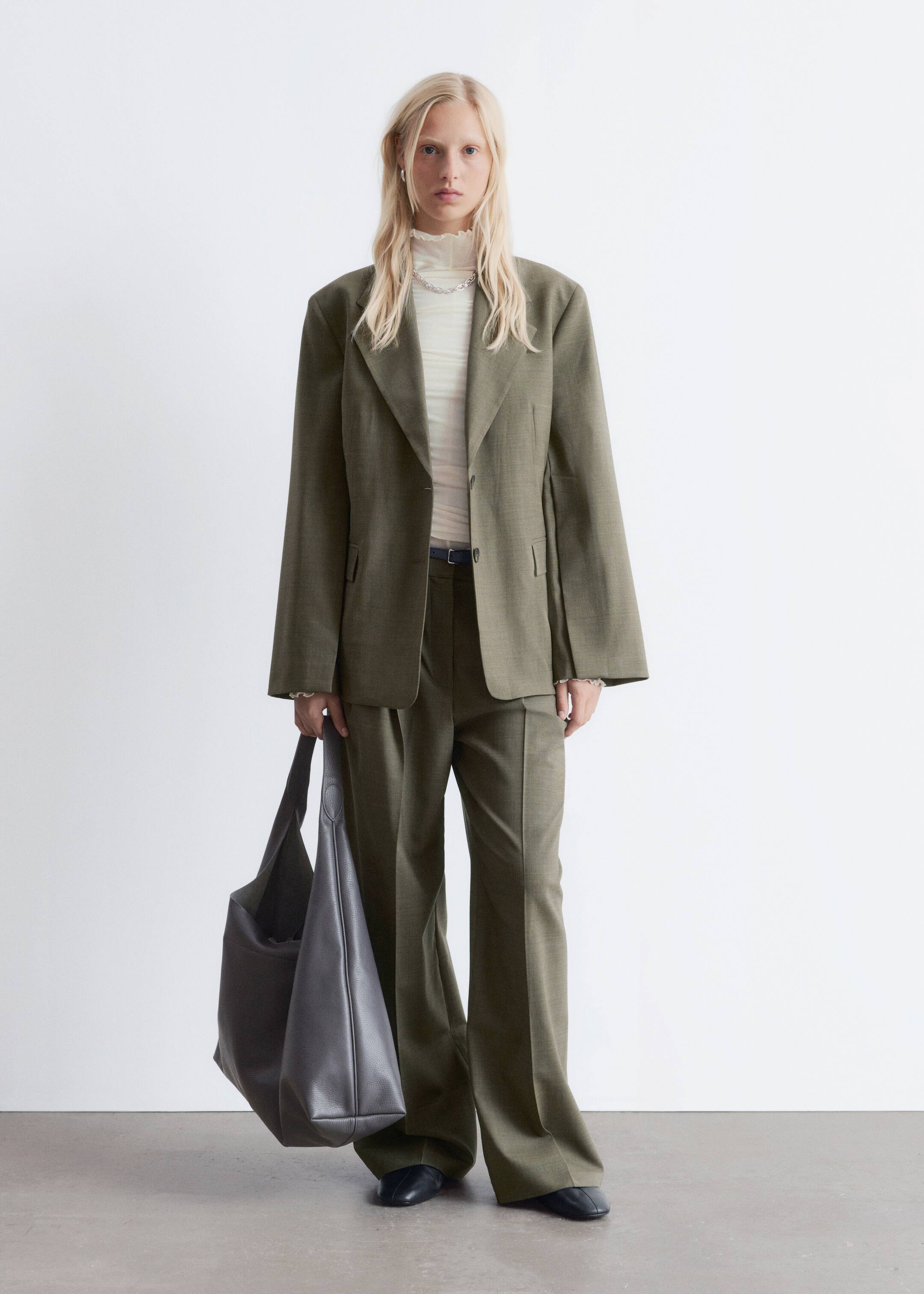 Visualizza immagine più grande: Un abito verde oliva è esposto da un'angolazione frontale, caratterizzato da un blazer oversize monopetto con spalle larghe e revers a dente. I pantaloni a gamba larga abbinati sono indossati con una cintura scura, e un top leggero, semi-trasparente, a collo alto con bordi arricciati è indossato sotto il blazer.