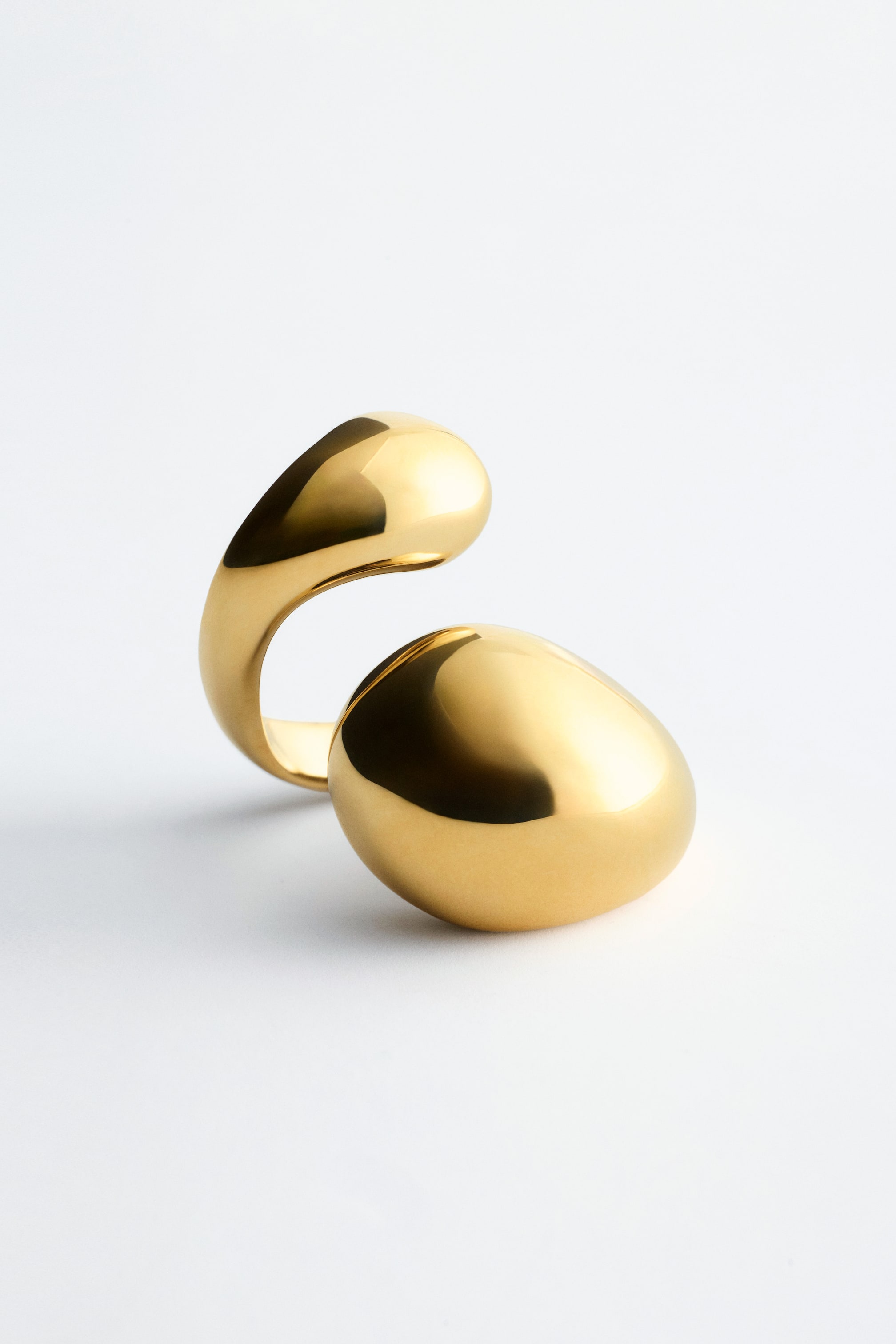 Größeres Bild ansehen: Ein offener Ring präsentiert ein elegantes, skulpturales Design aus hochglanzpoliertem Messing. Er zeichnet sich durch zwei glatte, abgerundete Formen aus, die sich biegen, um eine offene Lücke zu schaffen.
