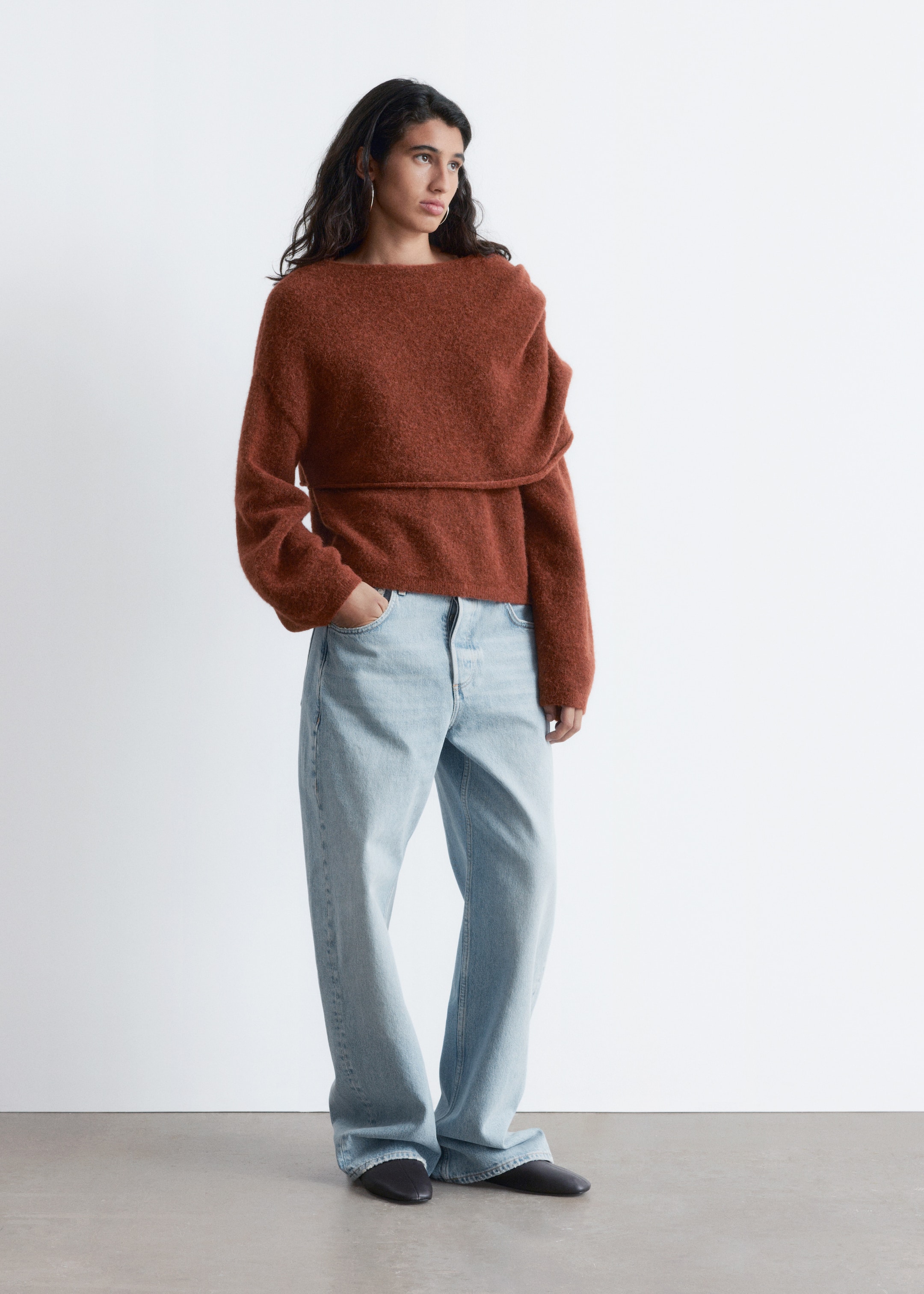 Se større billede: En rustfarvet, fuzzy bådhals sweater, med et bredt, vandret lagdelt design over brystet og lange ærmer, bliver præsenteret. Den er stylet med lyse, løstsiddende, højtaljede jeans, der samler sig ved anklerne over sorte spidse flade sko.