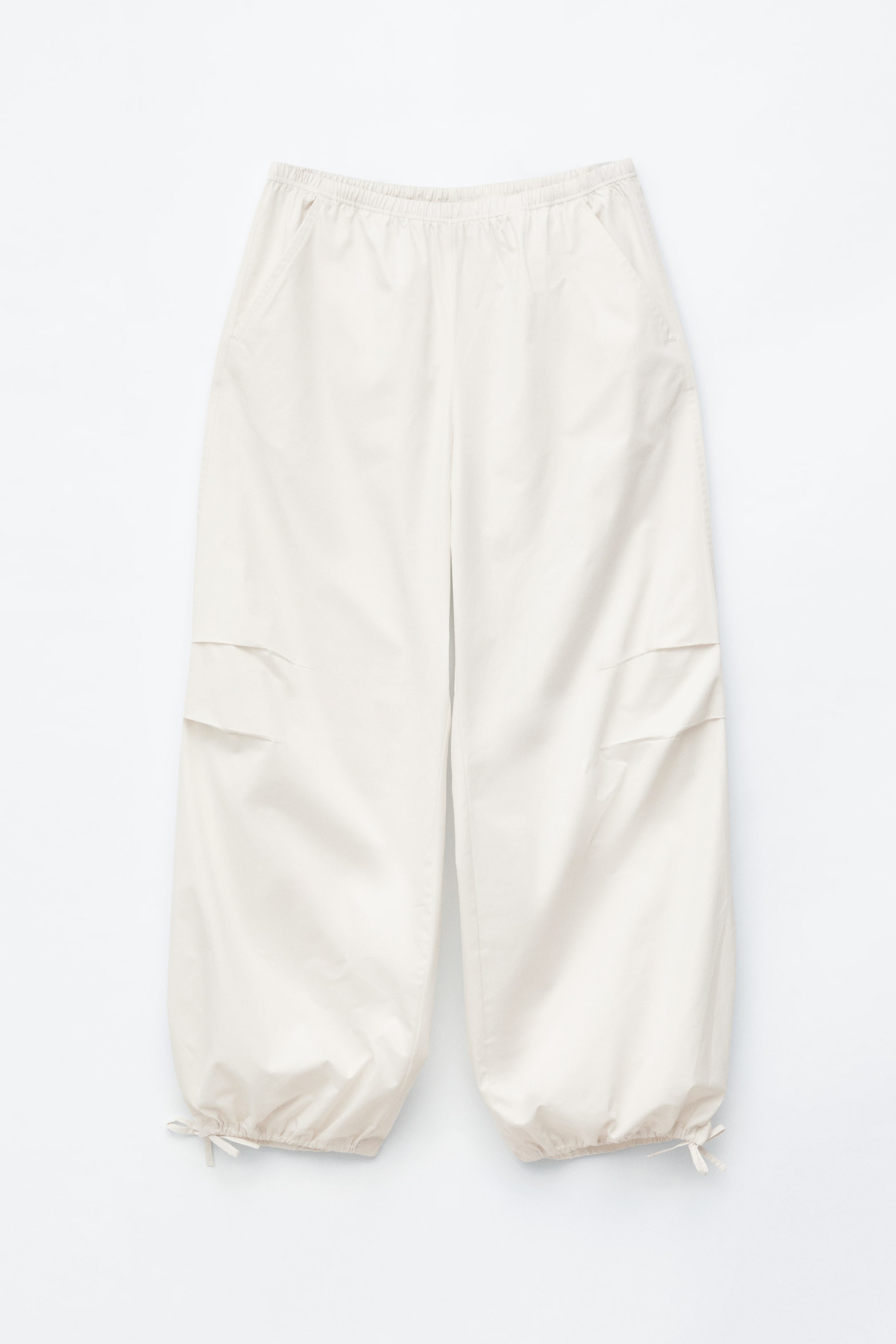 Vis større bilde: Lyse kremfargede cargobukser med avslappet passform, elastisk midje og sidesøm lommer. De har også klafflommer på lårene og snorstramming ved anklene, som gir en samlet kant.