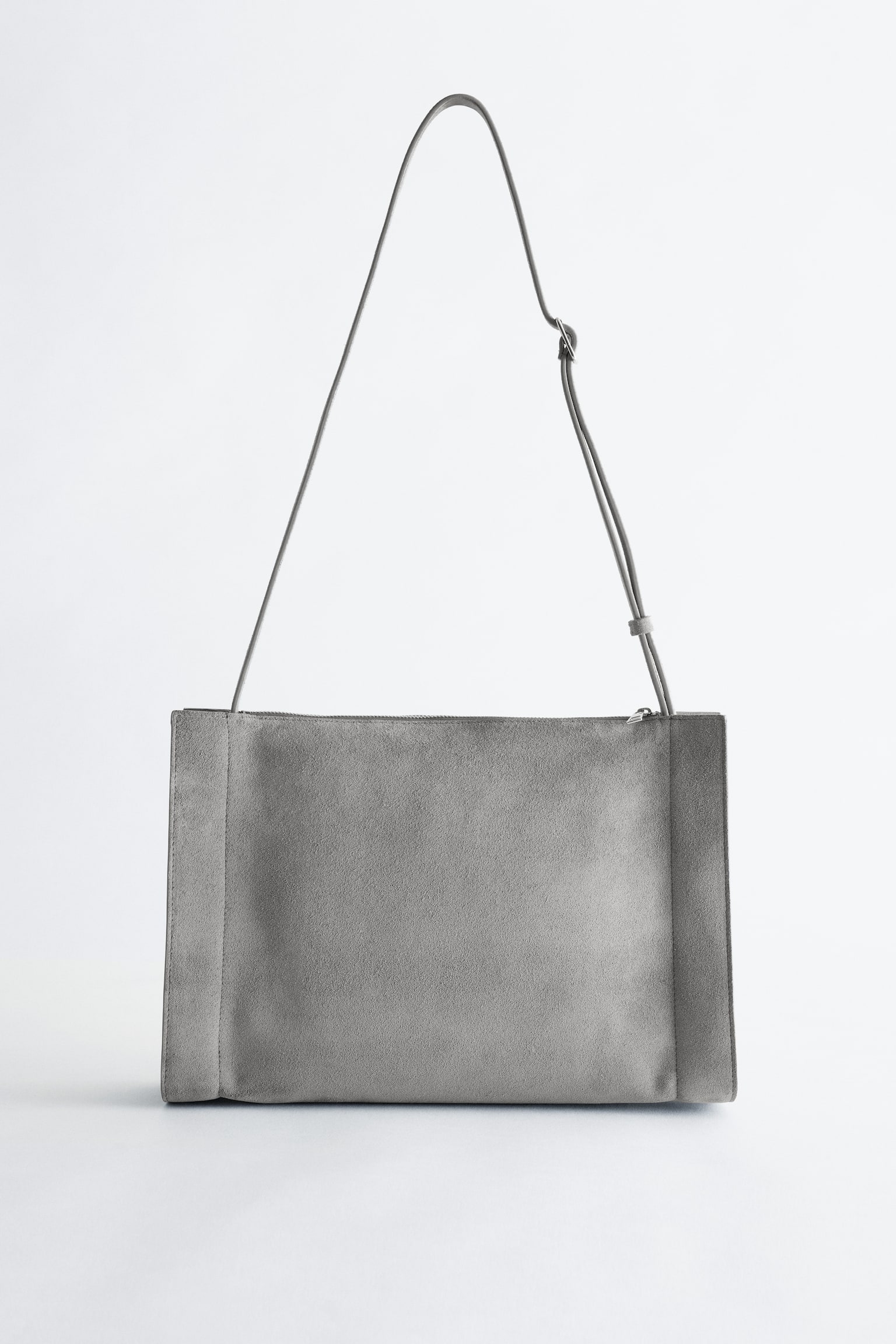 Μια γκρι τσάντα crossbody από διχασμένο σουέτ παρουσιάζει το ορθογώνιο μπροστινό της μέρος. Διαθέτει λεπτό, ρυθμιζόμενο λουράκι και κλείσιμο με φερμουάρ κατά μήκος της επάνω άκρης. - 1