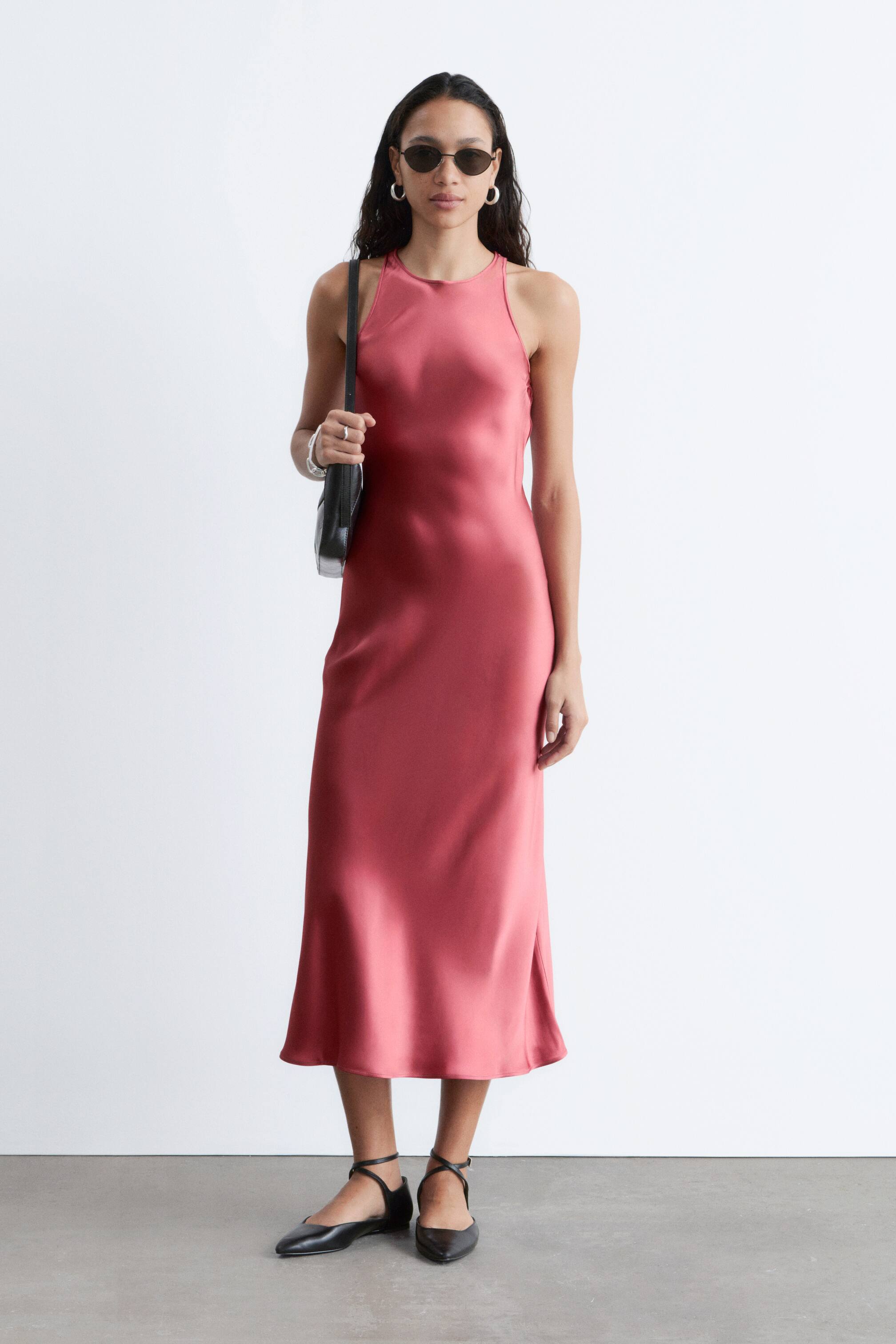 Vis større bilde: En dempet rosa midikjole i satengfinish med en høy halterneck, en flytende rett silhuett og en diskret sidesplitt.