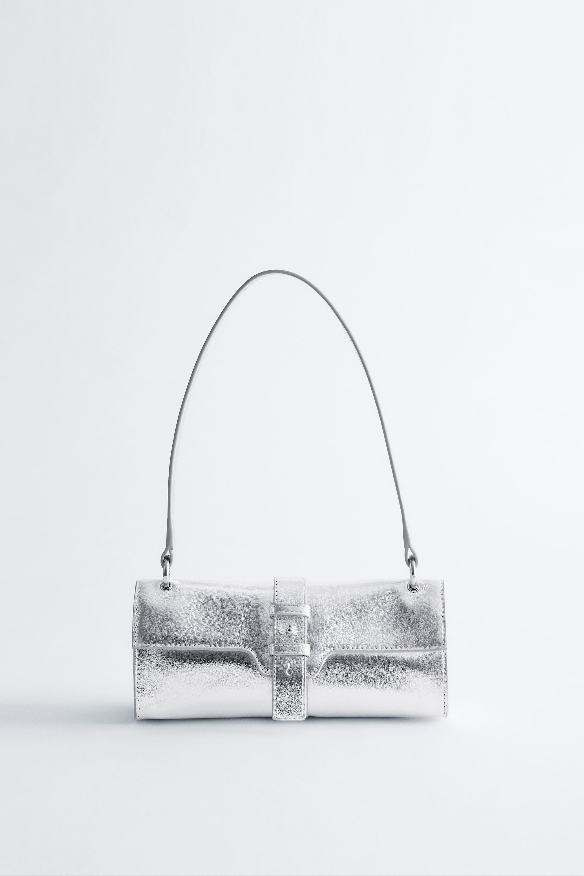Zobacz większy obraz: Srebrna metaliczna skórzana torebka na ramię jest pokazana z przodu, charakteryzująca się wydłużonym prostokątnym kształtem i płaską rączką. Jej przednia klapa zamykana jest na srebrną klamrę i pasujący pasek.