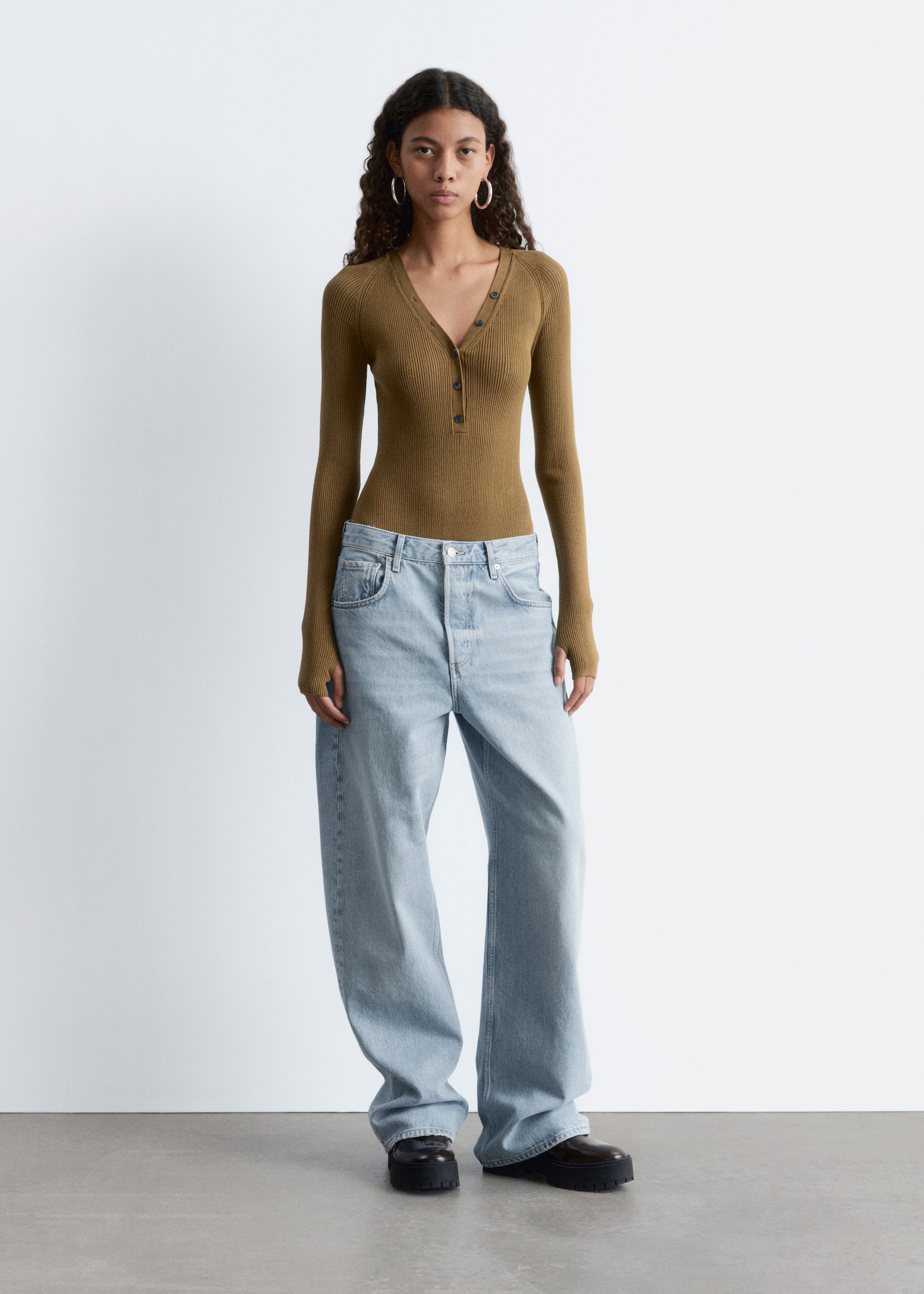 View larger image: A fitted olive green ribbed henley top, featuring a V-neck and a partial button placket with dark buttons, is being worn from a front angle, tucked into light-wash, wide-leg denim jeans. The jeans are pooling over black chunky-soled shoes.