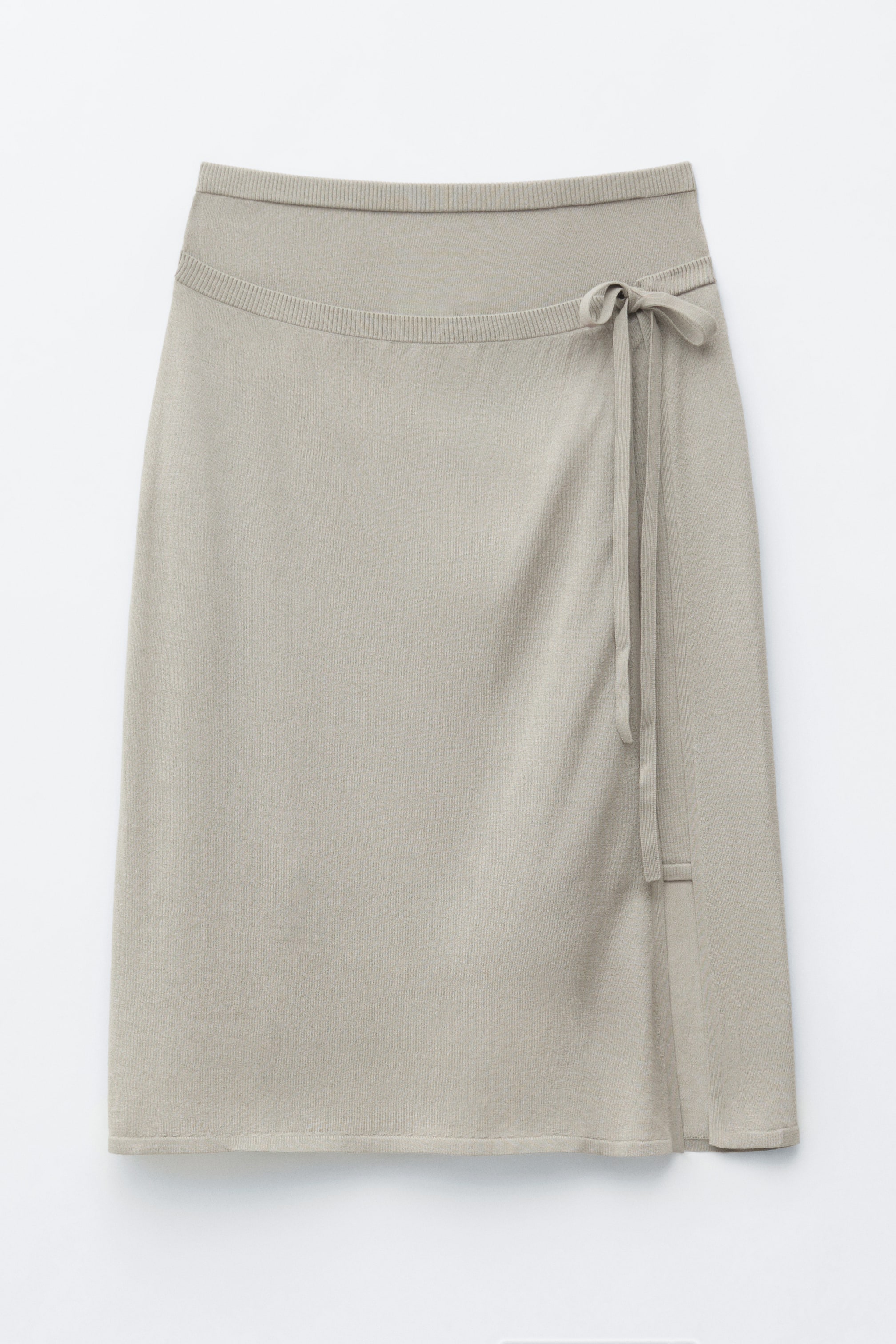 Ver imagen más grande: Una falda midi de punto fino en color beige claro se muestra desde el frente, con una cintura acanalada y una silueta envolvente asimétrica que se ata en el lado derecho con un lazo, creando un efecto de panel frontal en capas.