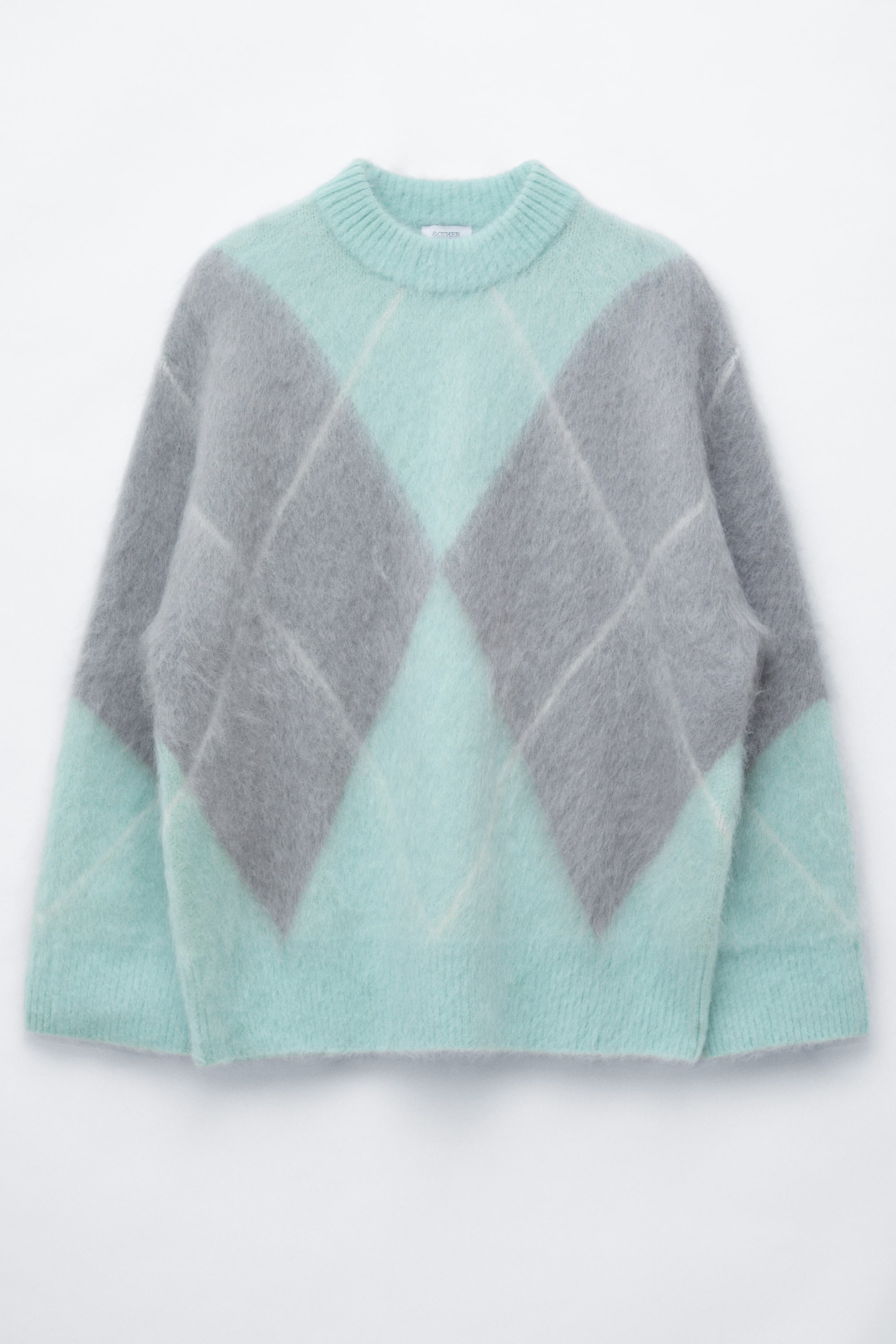 Zobacz większy obraz: Sweter z domieszką moheru jest pokazany z przodu, z oversize’ową sylwetką i wzorem argyle jacquard w kolorze miętowej zieleni i szarości. Sweter prezentuje puszystą, miękką dzianinę z prążkowanym okrągłym dekoltem, prążkowanymi mankietami i prążkowanym dołem.