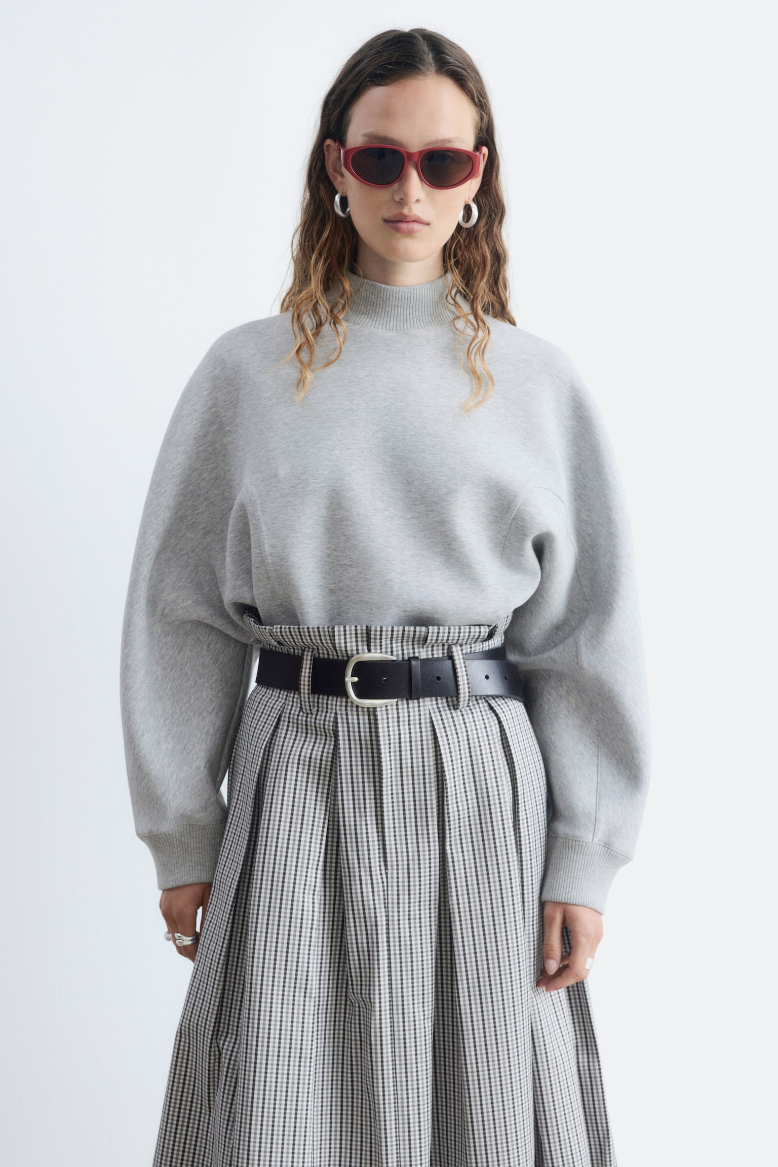 Una sudadera gris claro muestra su parte frontal, con un cuello simulado acanalado y hombros caídos. Las mangas largas terminan en puños acanalados, y los detalles de costura curvada acentúan la parte superior del torso frontal, justo por encima de un dobladillo ancho acanalado que completa el cuerpo recortado. - 1