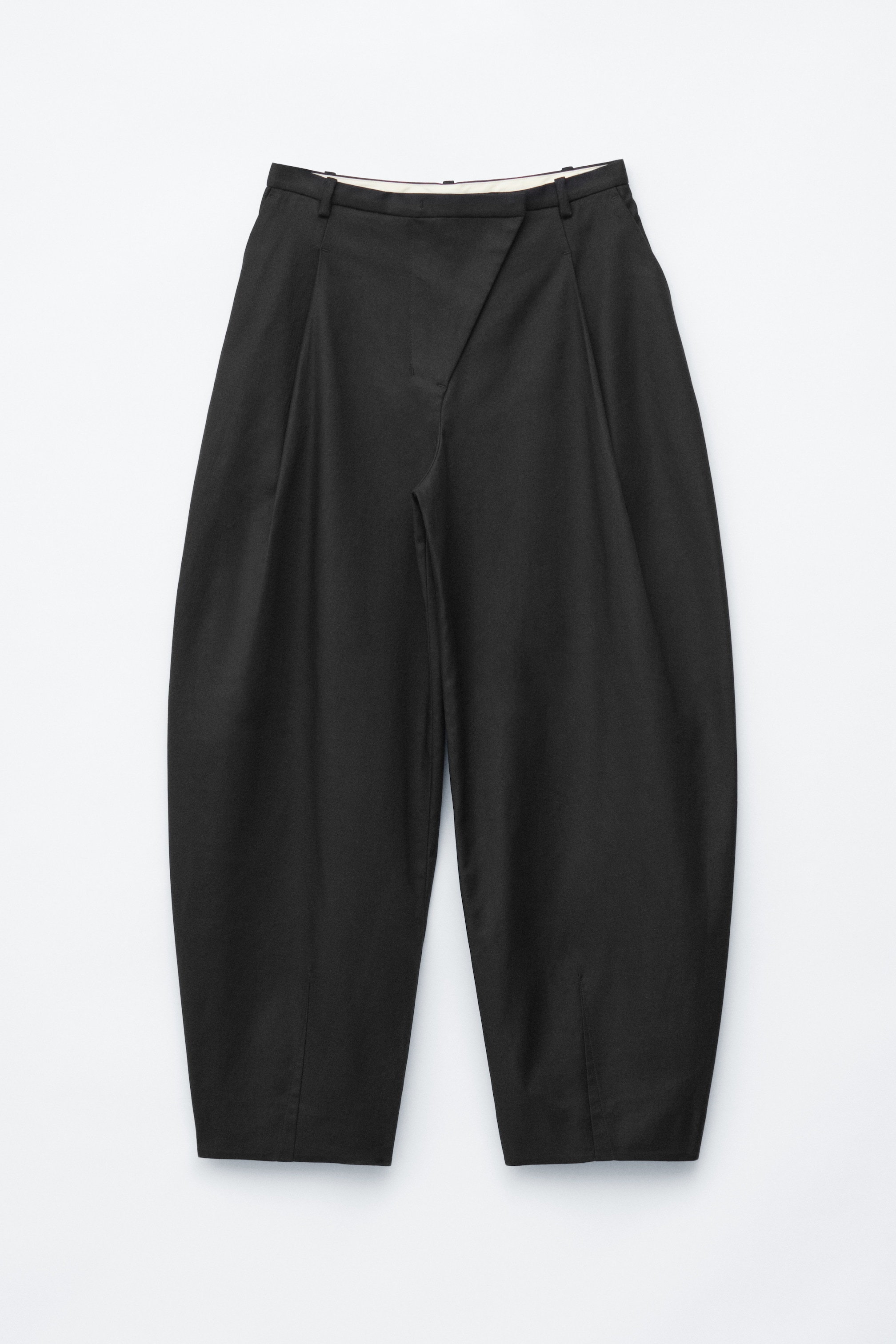 Größeres Bild ansehen: Schwarze Hosen werden flach von vorne präsentiert, mit einer lockeren Passform und langen, fassförmigen Beinen, die durch Kellerfalten akzentuiert werden. Ein schräger Hosenverschluss ist an der Taille sichtbar.