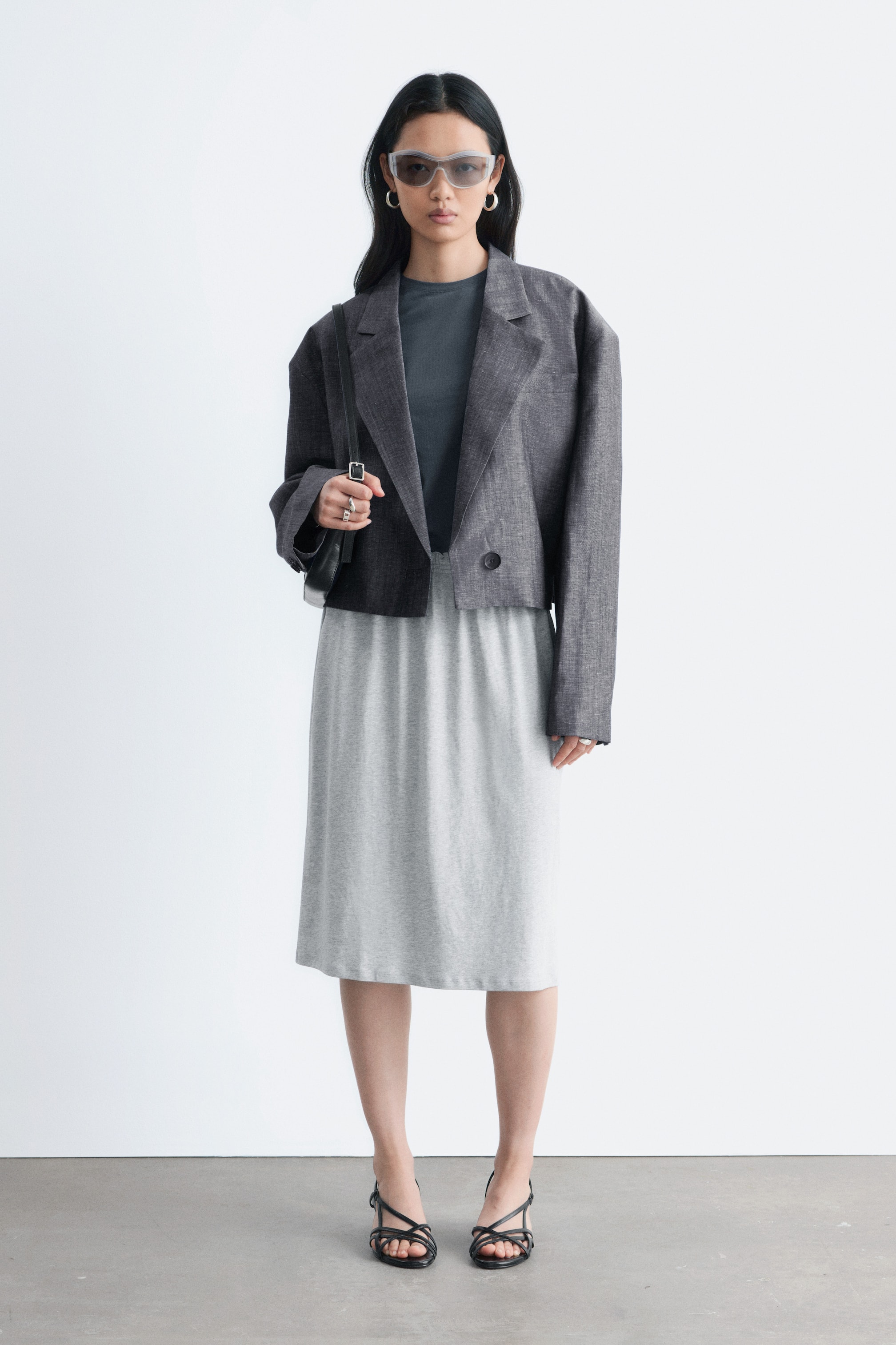 Προβολή μεγαλύτερης εικόνας: Η μοντέλο φοράει μια ανοιχτό γκρι φούστα μέχρι το γόνατο από ζέρσεϊ. Η φούστα διαθέτει ελαστική, σμικρυνόμενη ζώνη μέσης, η οποία καλύπτεται μερικώς από ένα σκούρο γκρι κοντό σακάκι.