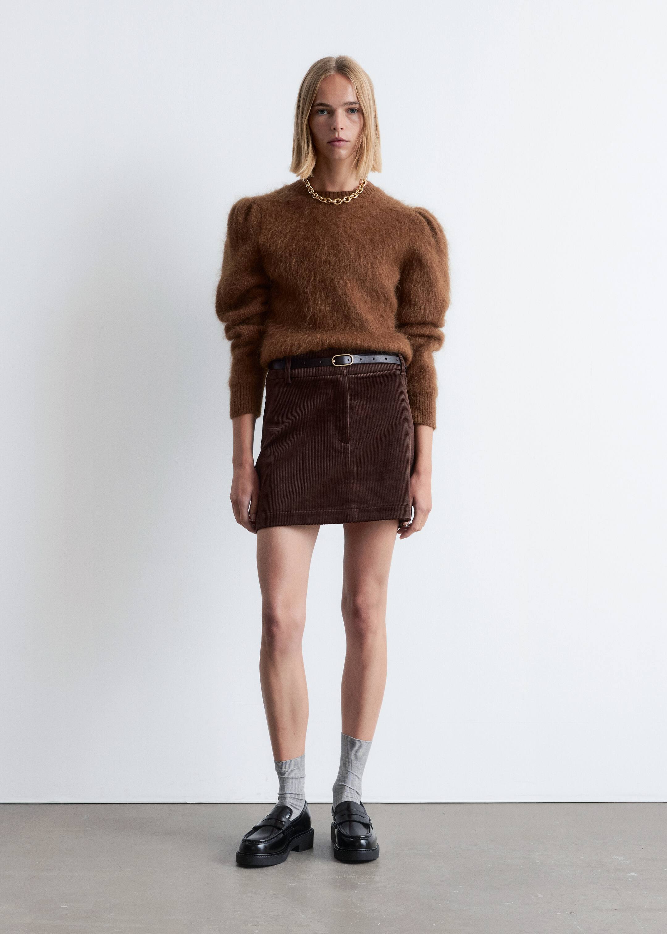 View larger image: A brown fuzzy sweater with voluminous puffed sleeves is being worn with a dark brown corduroy mini skirt, cinched by a thin black belt with a gold-toned buckle. Black chunky loafers are being worn with light gray ribbed socks, and a gold-toned chunky chain necklace is resting on the sweater's neckline.