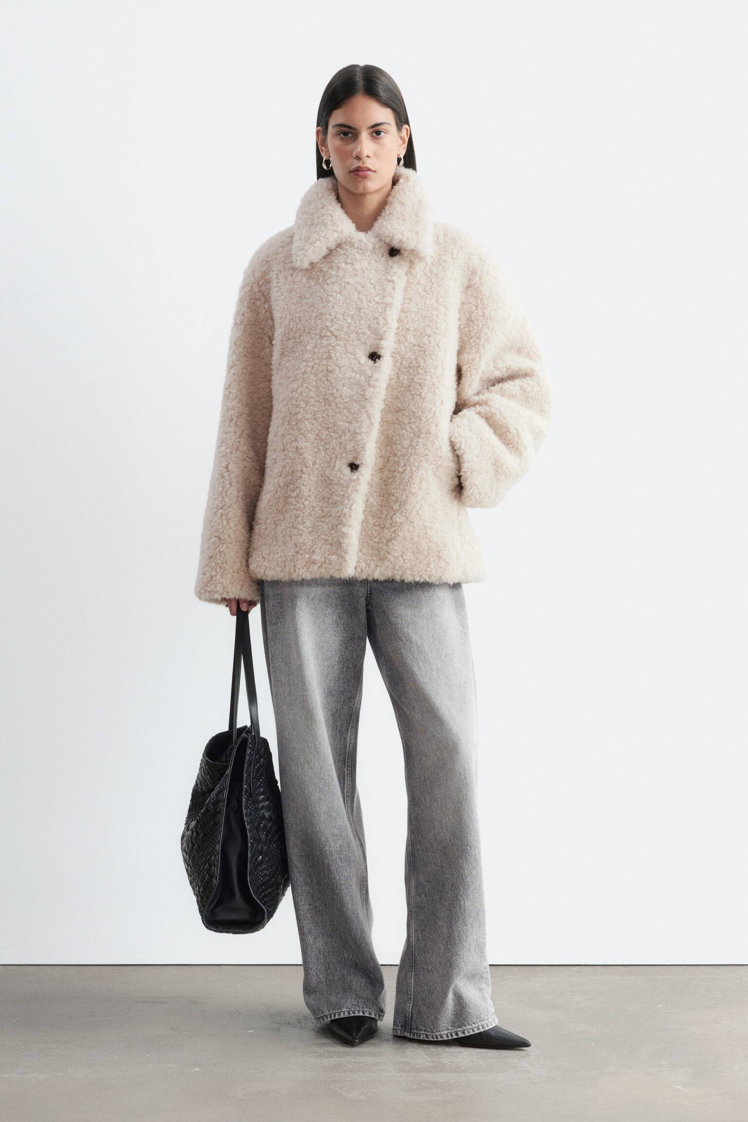 Eine hellbeige Kunstpelzjacke wird von vorne präsentiert, mit einem klassischen Umlegekragen und einer schrägen Knopfleiste mit zwei dunklen Knöpfen. - 1