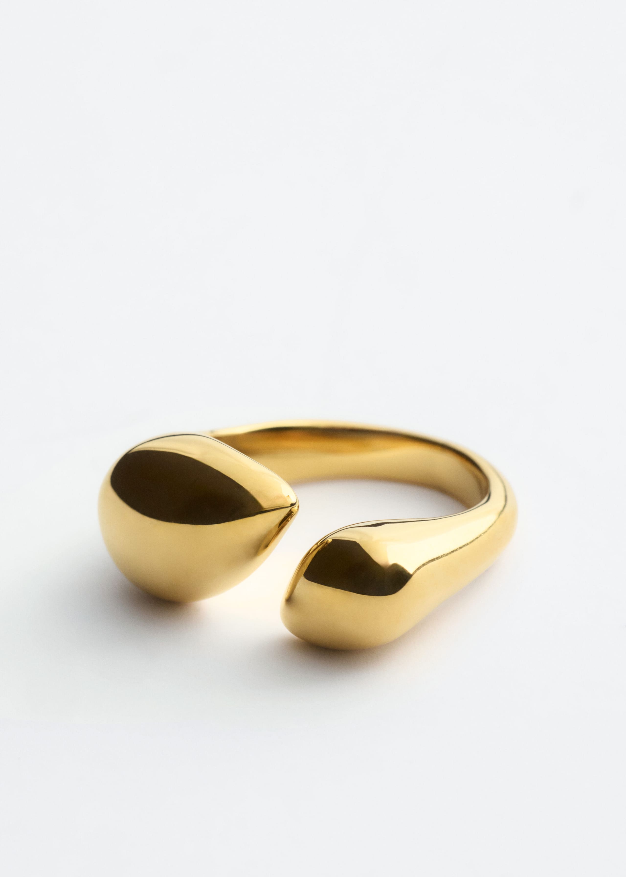 Dieser polierte Messingring präsentiert ein offenes Design mit zwei glatten, bauchigen, tropfenförmigen Enden, die einander entgegengebogen sind. Der Ring ist frontal ausgerichtet und betont seine reflektierende, hochglänzende Goldoberfläche sowie seine organische, fließende Silhouette.