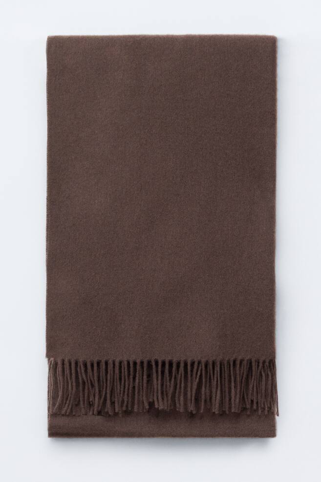 A large brown wool blanket scarf is lying flat, showcasing its soft, textured surface and a fringe trim along one end. - 1